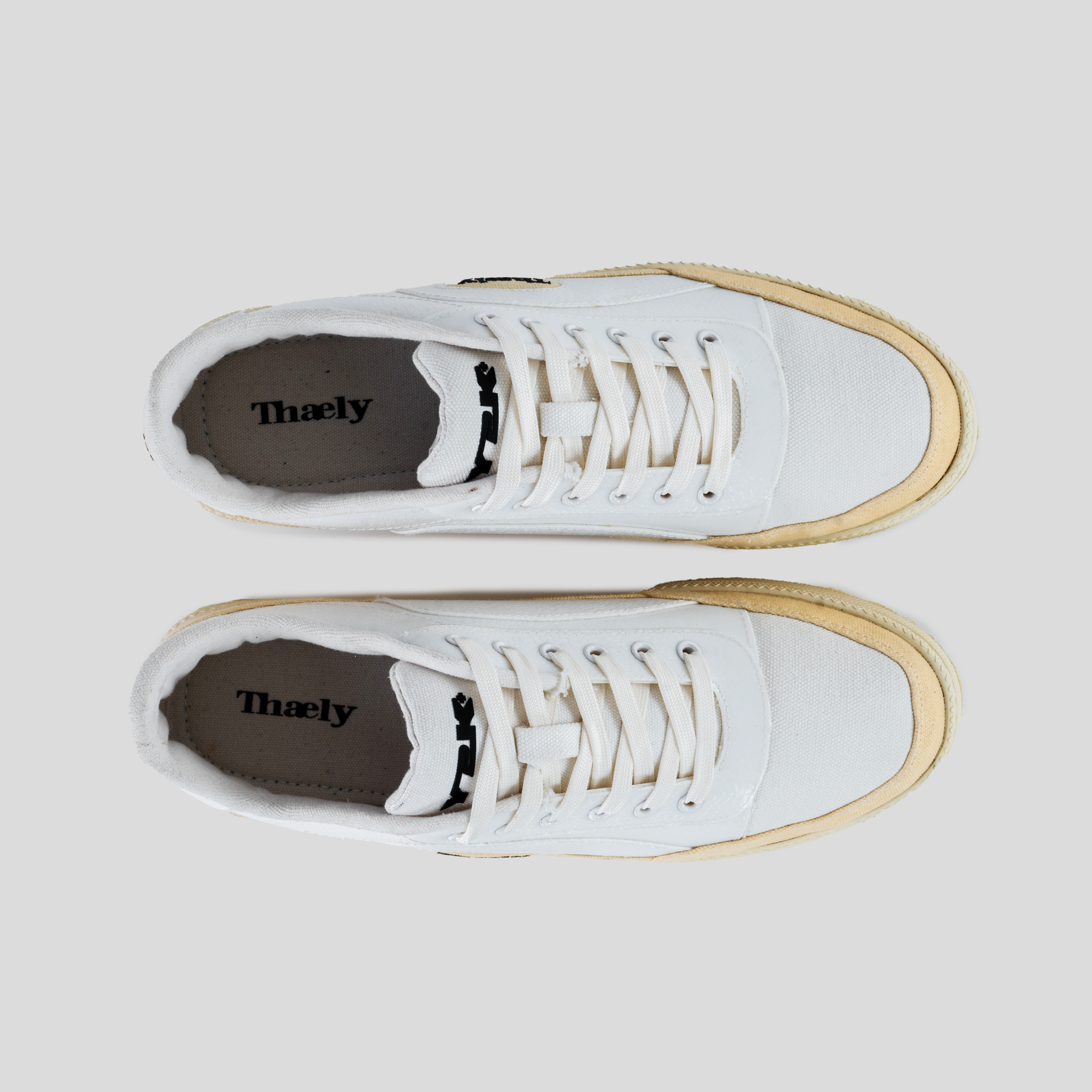 Top view of white canvas streetwear sneakers with off-white soles and laces on gray background