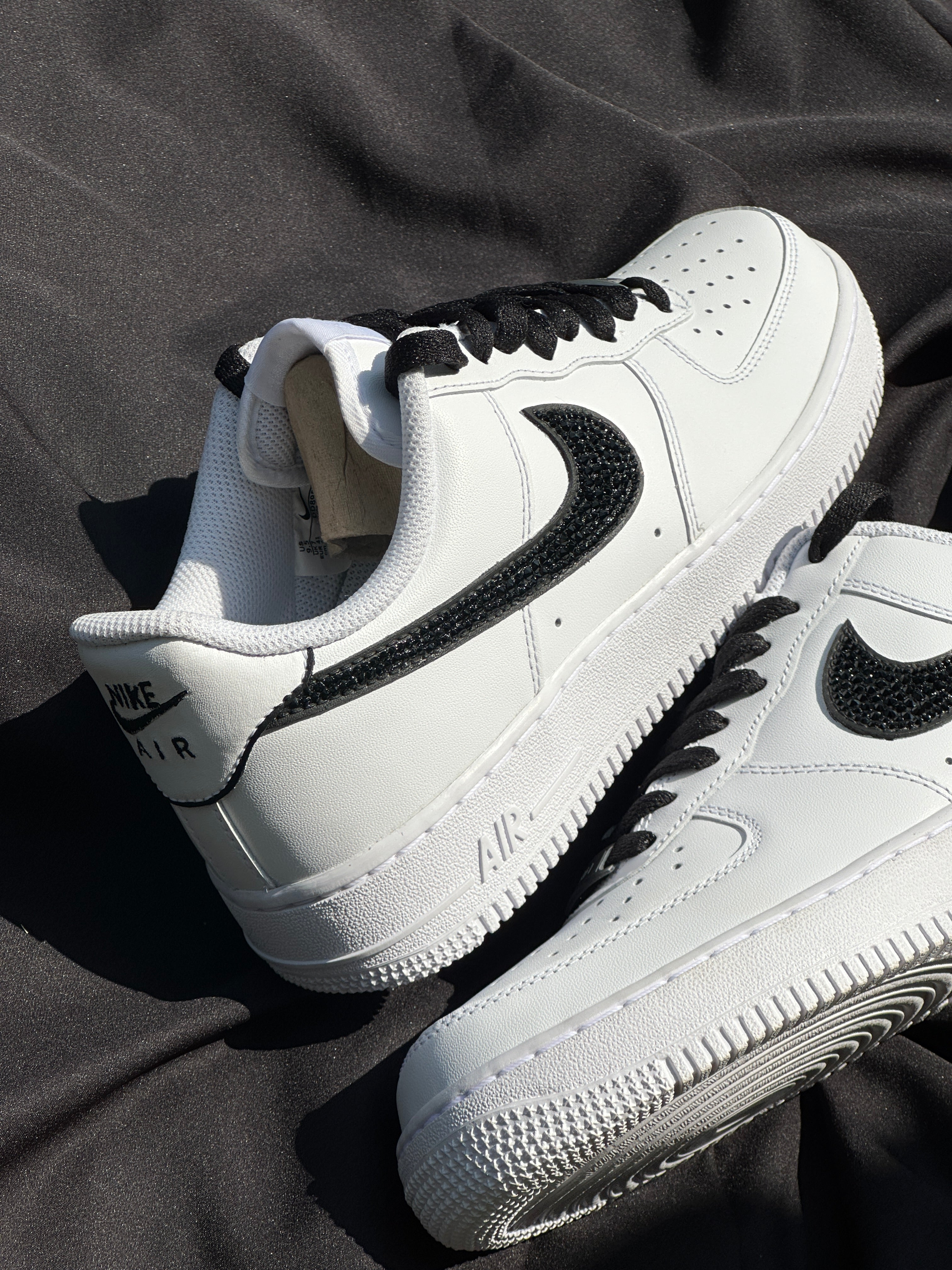 White Nike Air Force 1 sneakers with black swoosh and laces on black fabric