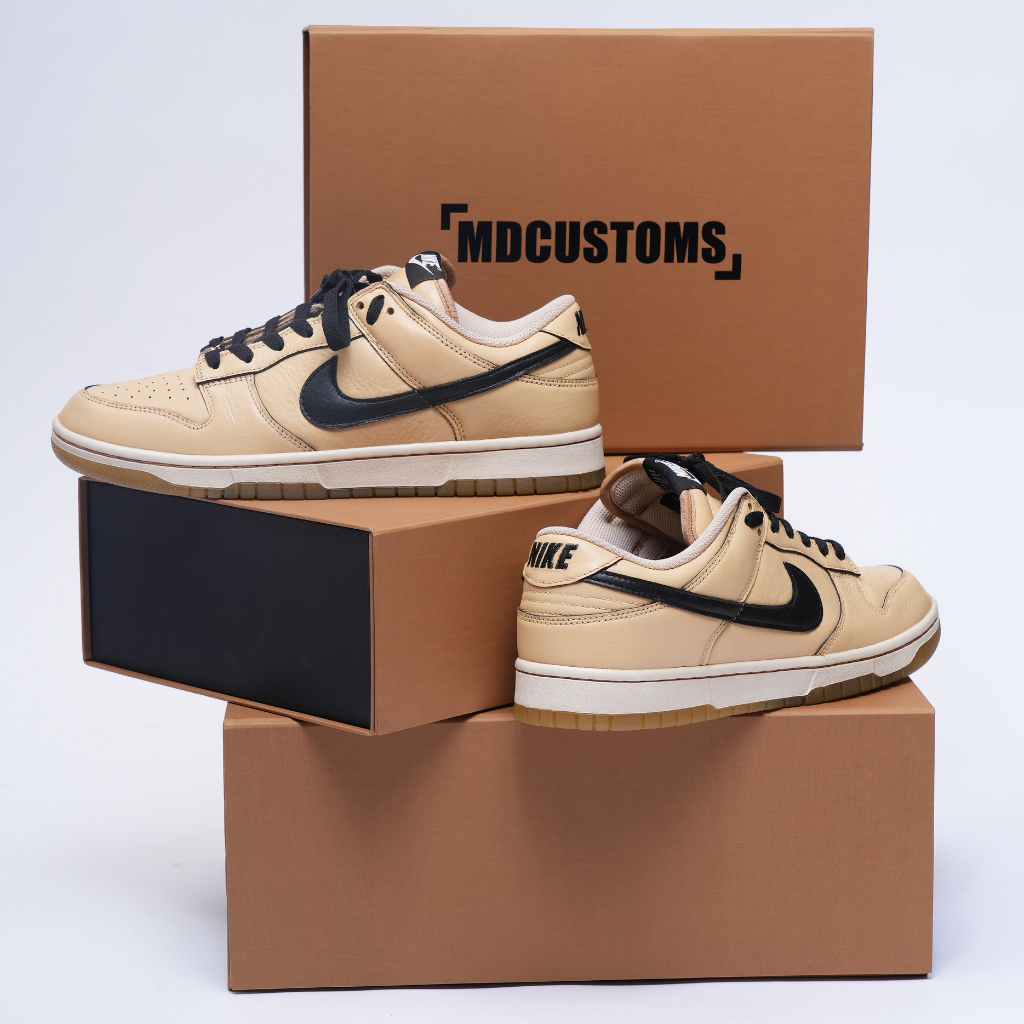 Tan and black Nike Dunk Low sneakers displayed on stacked brown shoeboxes, streetwear footwear