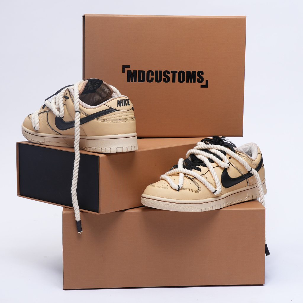 Beige and black Nike Dunk Low sneakers with thick rope laces displayed on brown shoeboxes