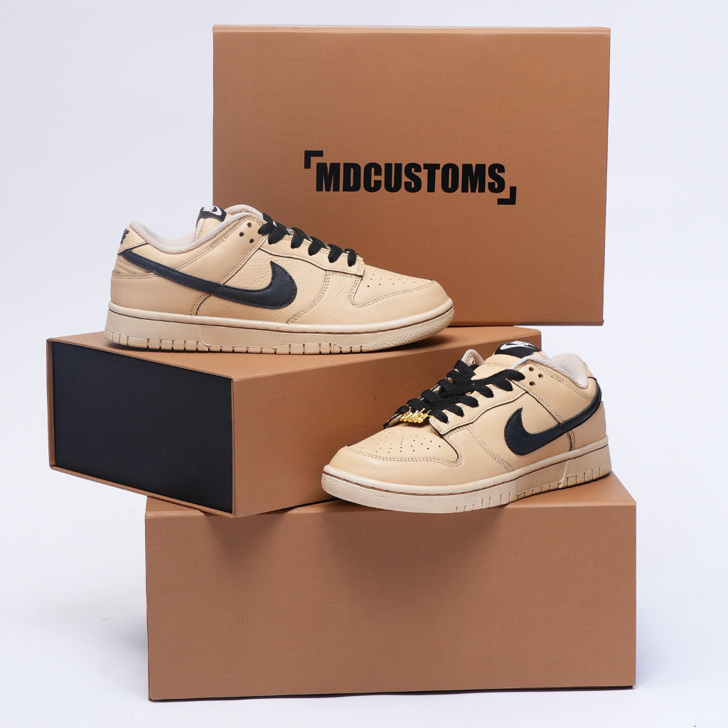 Beige and black Nike Dunk Low sneakers displayed on stacked brown shoe boxes