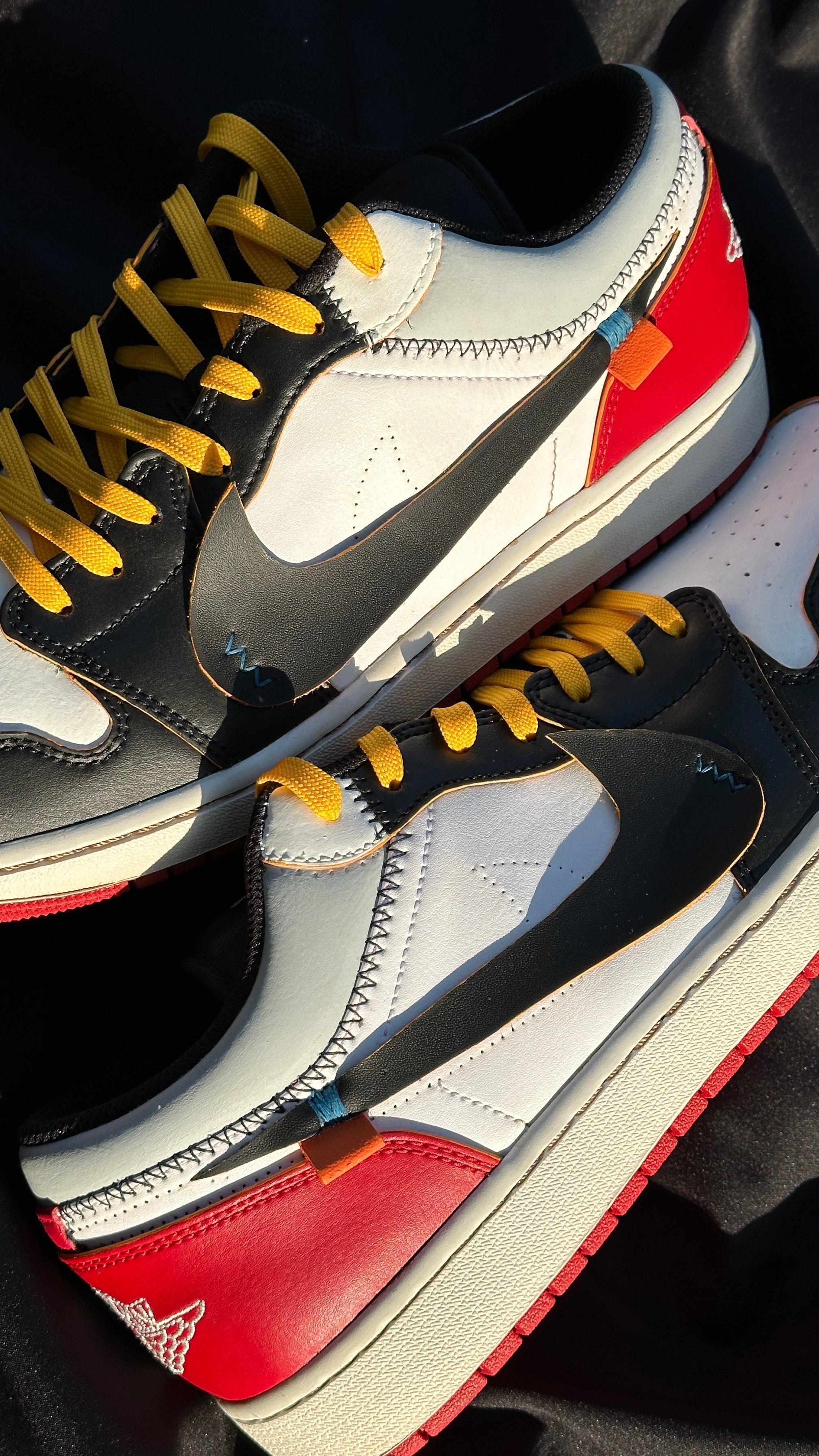 Close-up of limited edition low-top sneakers with yellow laces, black swooshes, red and white leather panels on a dark background.