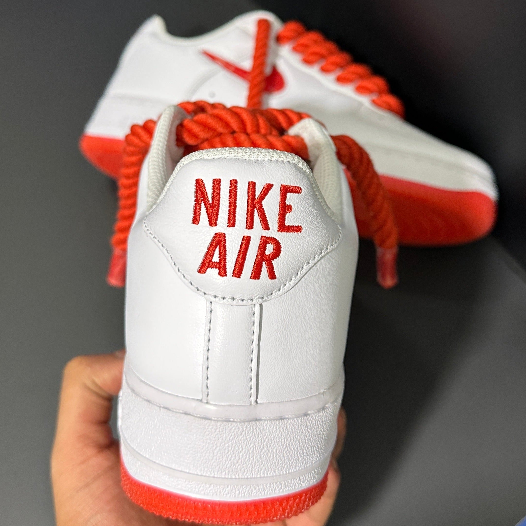 White Nike Air Force 1 sneaker with red accents and bold red laces, rear view