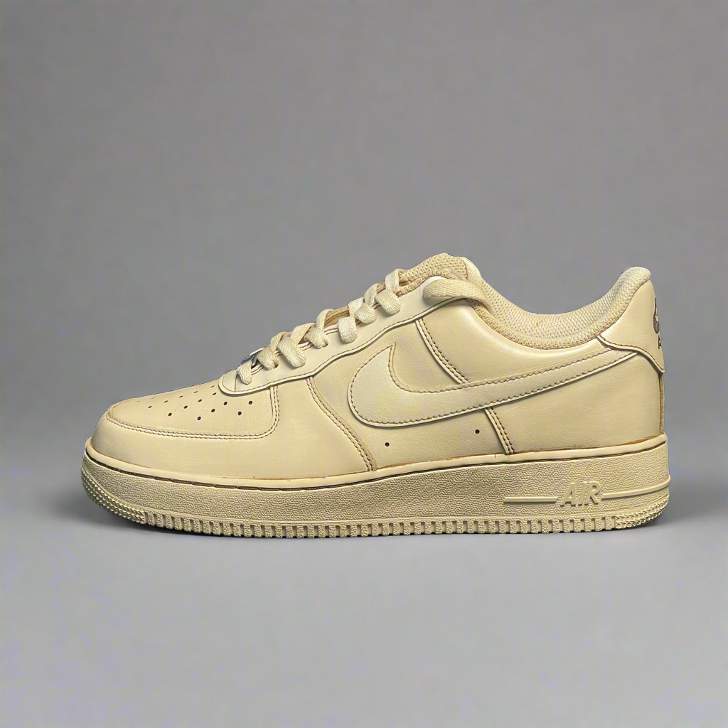 Beige low-top leather sneaker, side view, with perforated toe and rubber sole on gray background