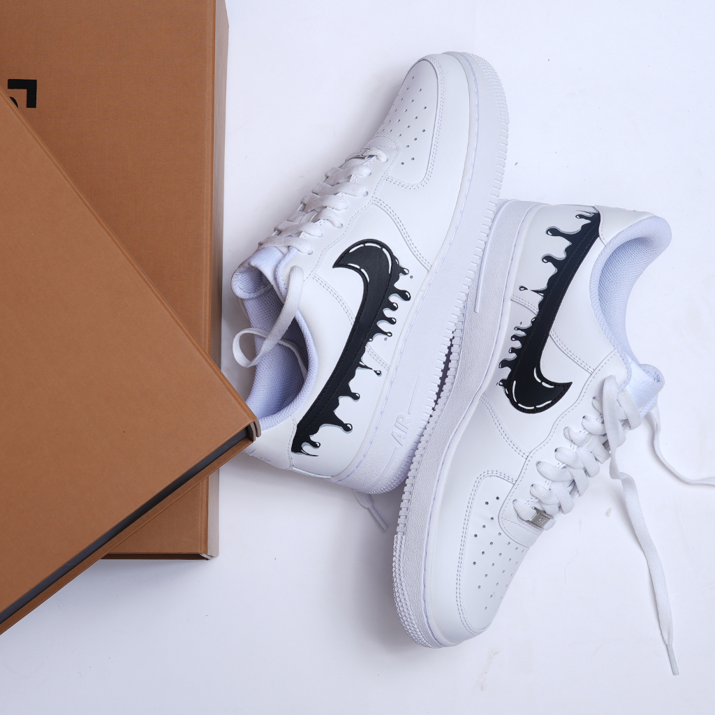 White streetwear sneakers with black drip swoosh design beside brown shoe boxes