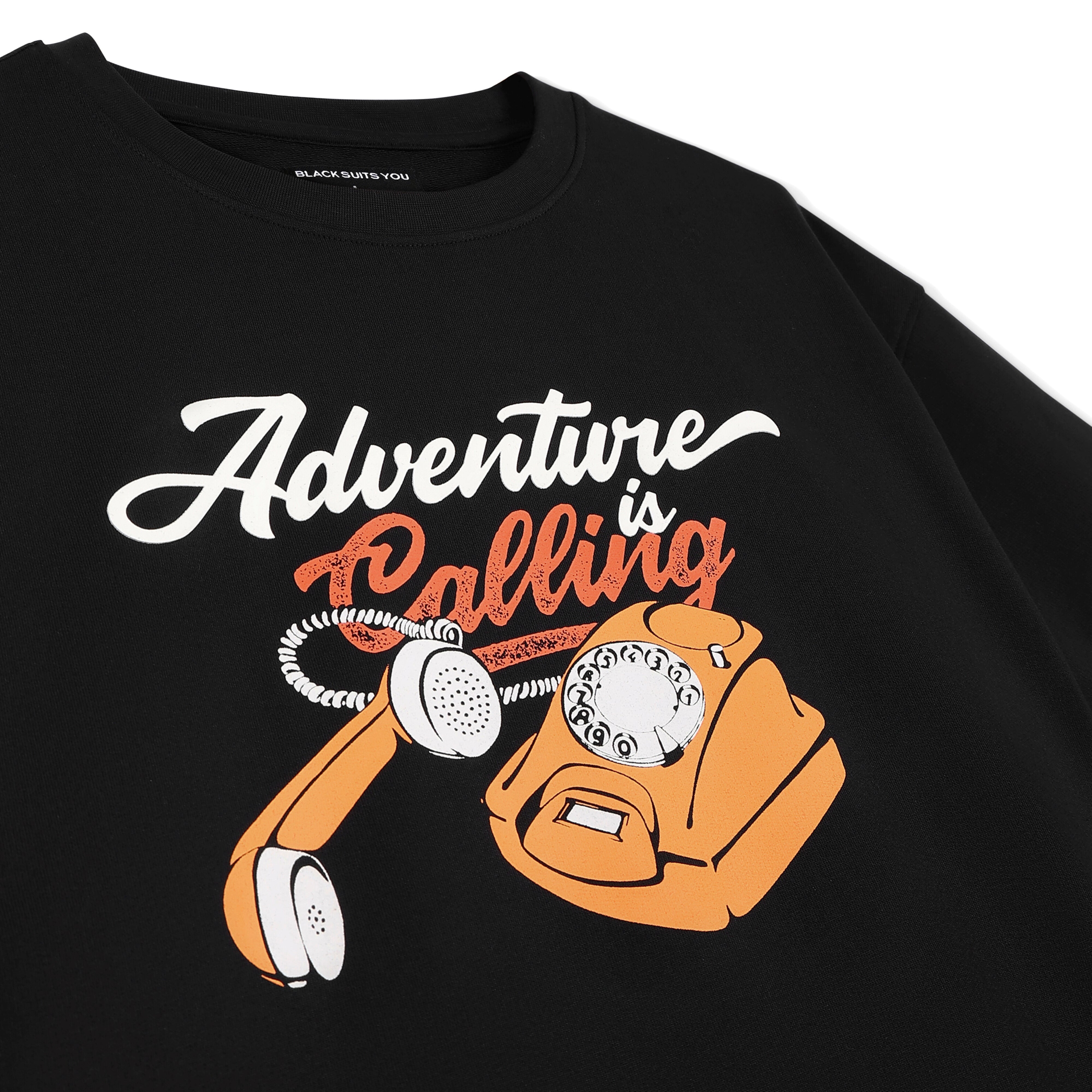 Black streetwear t-shirt with 'Adventure is Calling' text and orange retro rotary phone graphic.