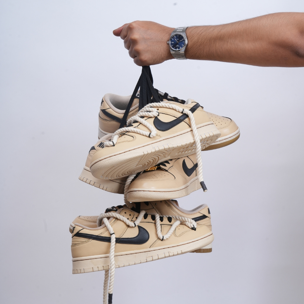 Hand holding beige and black Nike Dunk low sneakers with rope and black laces, streetwear style