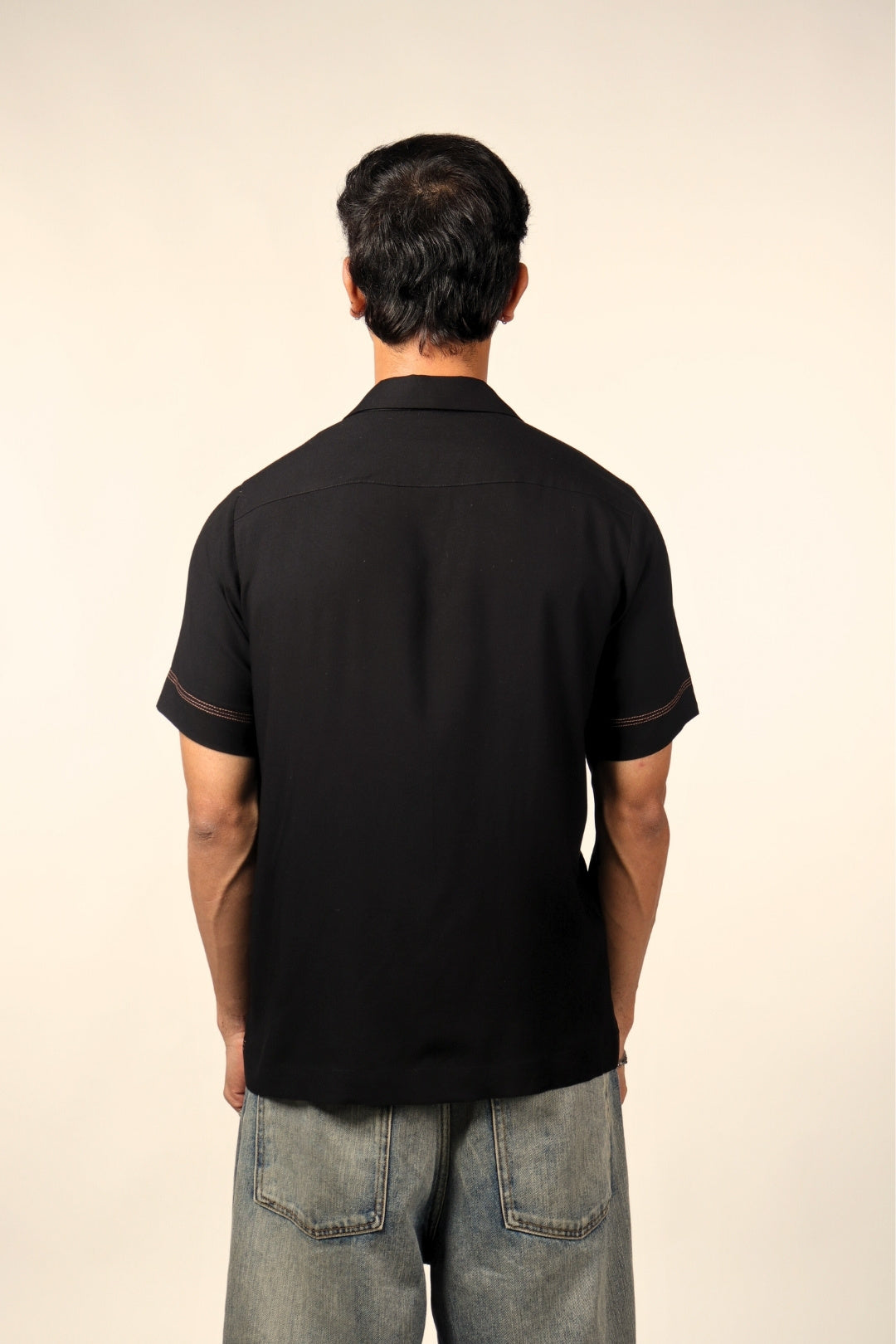 Man wearing black short sleeve shirt and blue jeans, viewed from the back