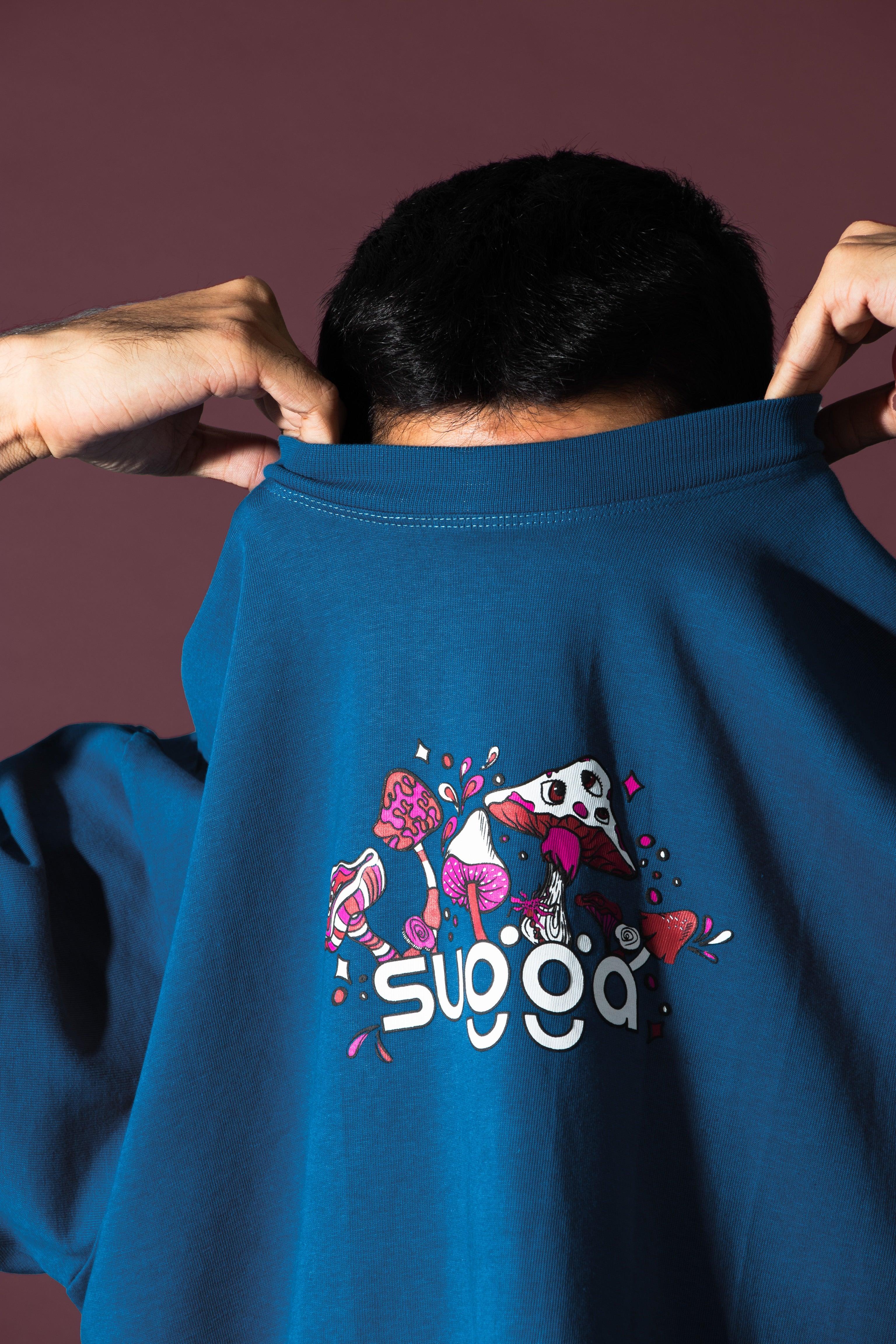 Person pulls blue streetwear t-shirt over face with colorful mushroom graphic and bold text
