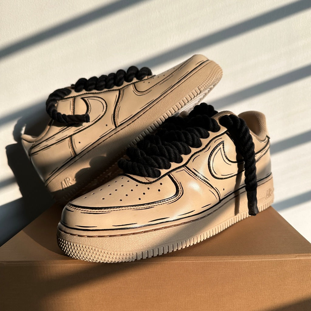 Beige streetwear sneakers with black sketch details and thick black laces on a box