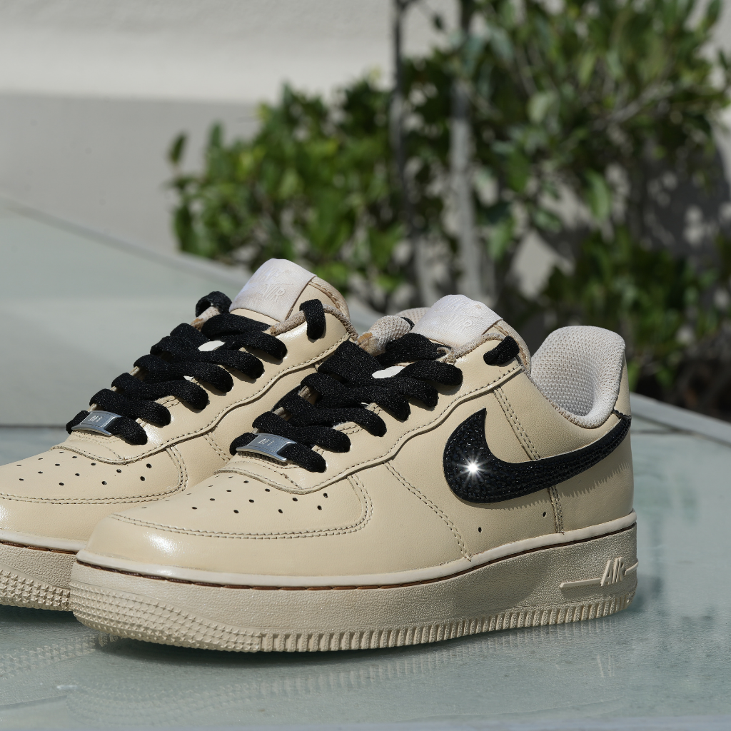 Beige Nike Air Force 1 sneakers with black swoosh and laces on outdoor glass surface