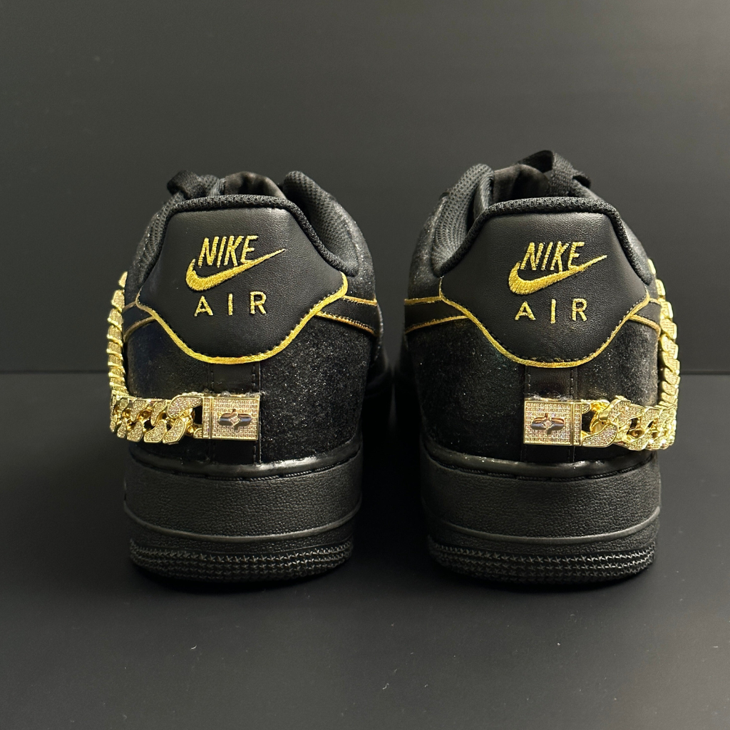 Black Nike Air sneakers with gold accents and chain details on the heel against black background