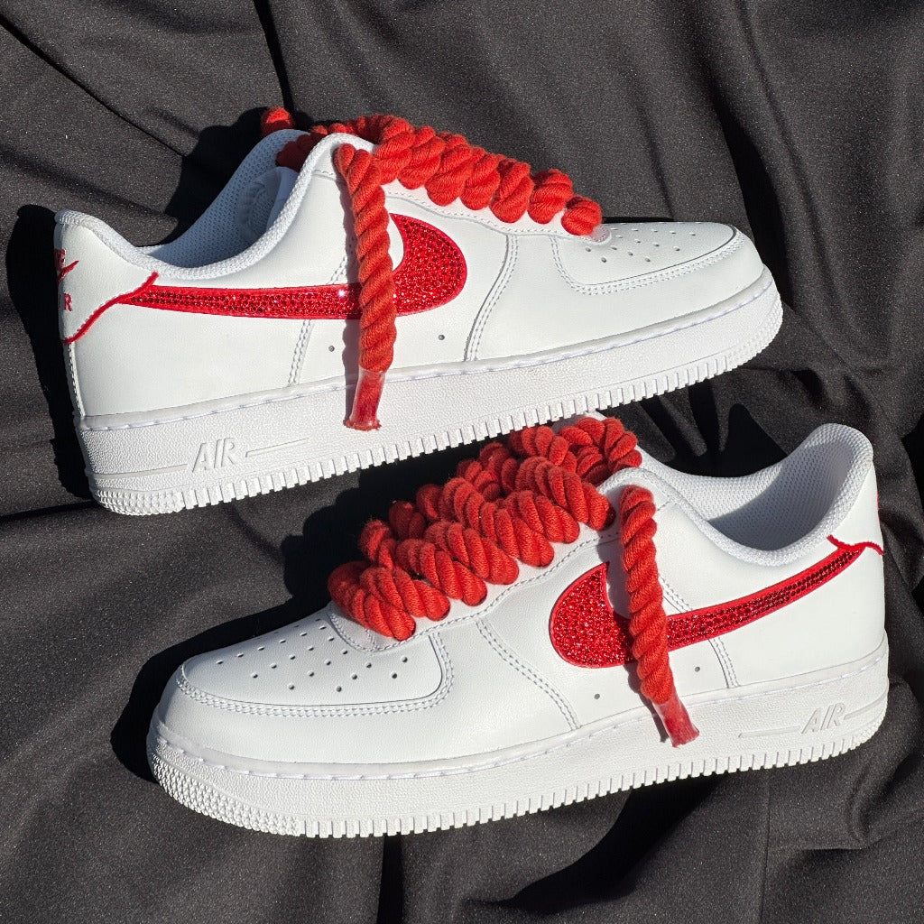 White low-top sneakers with red textured swoosh and thick red laces on black fabric