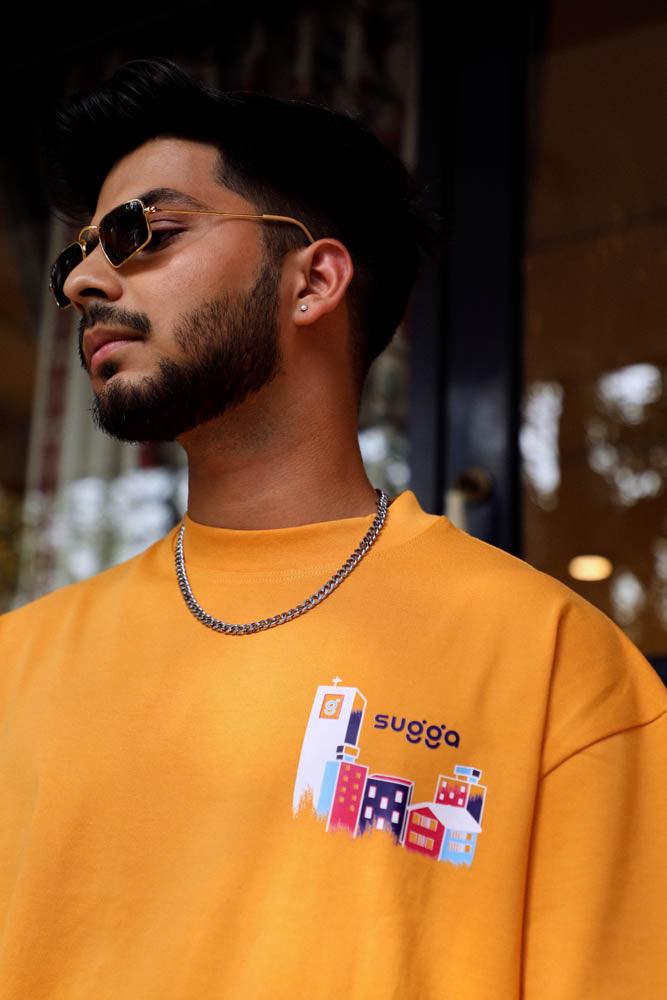 Man wearing yellow streetwear T-shirt with city graphic, chain necklace, and sunglasses