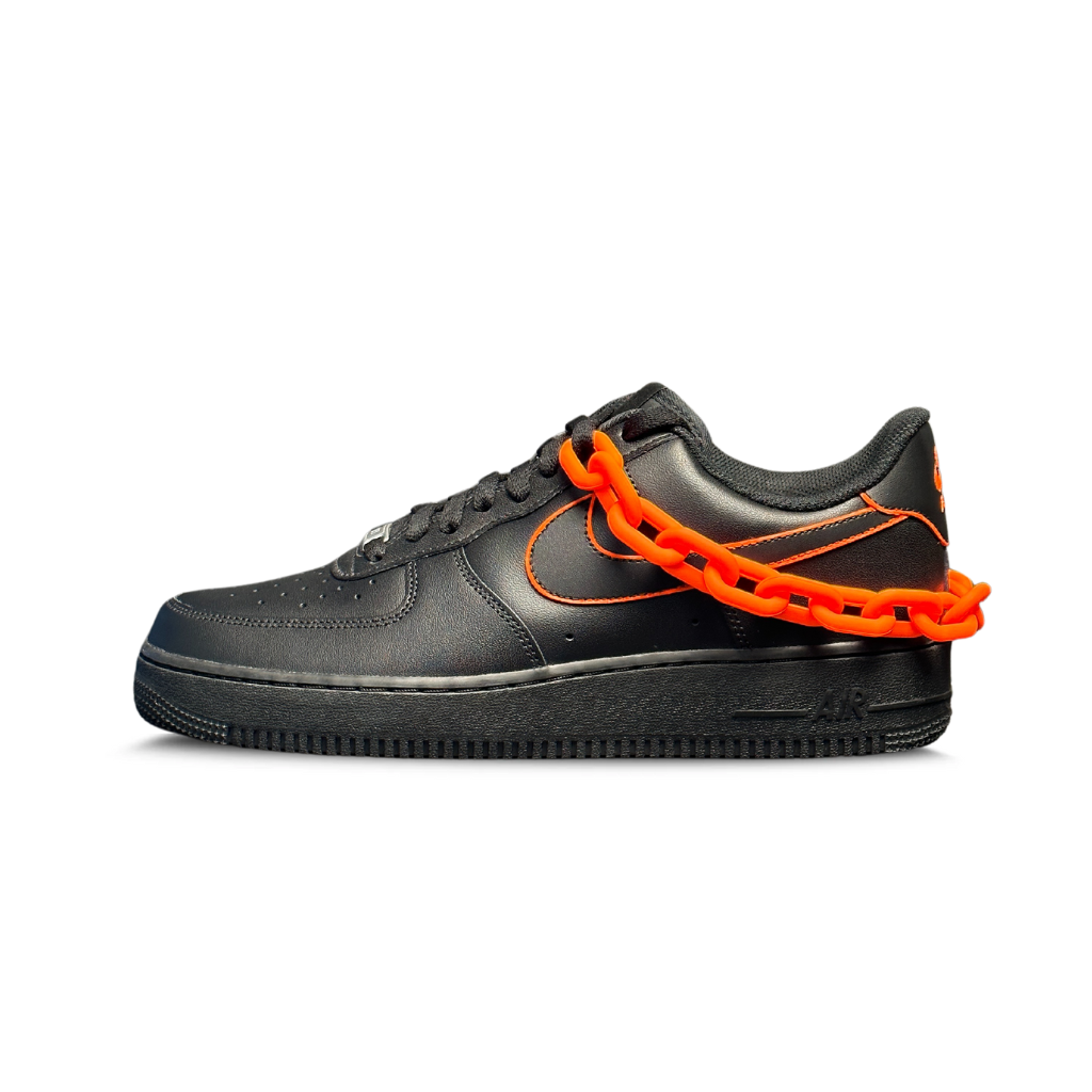 Black streetwear sneaker with orange stitching and bold orange chain accent on white background
