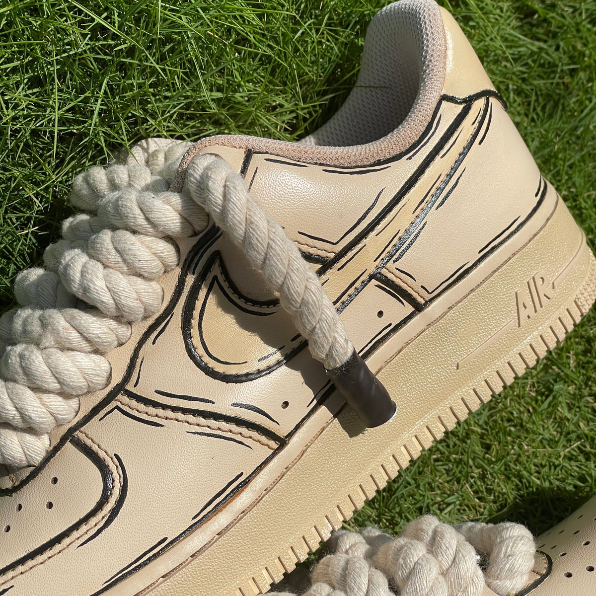 Beige sneaker with black outlined design, thick rope laces, on green grass