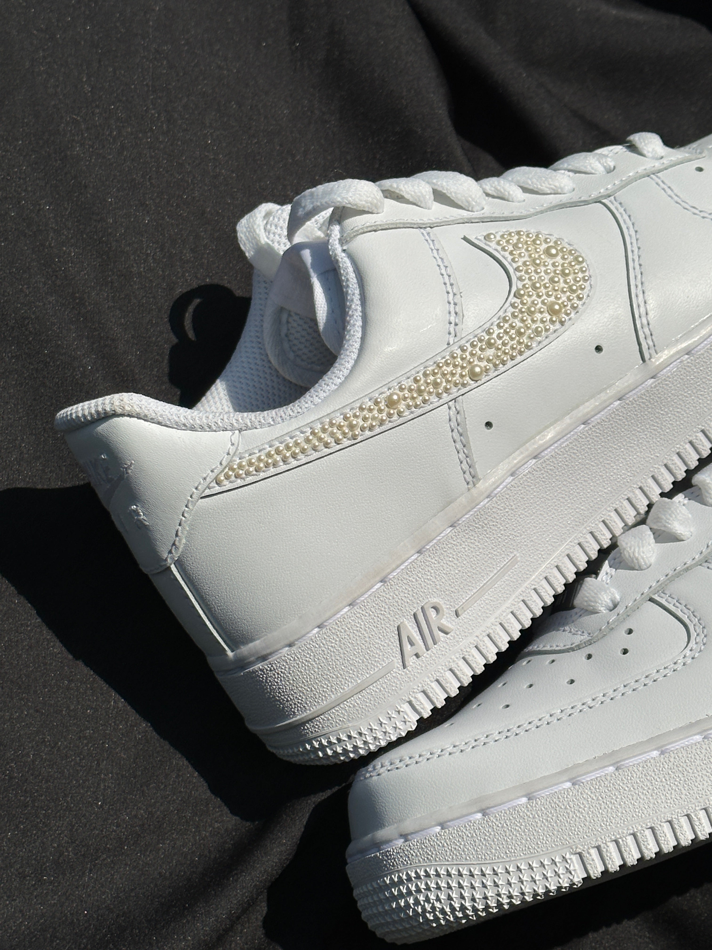 White sneaker with pearl-studded Swoosh logo, luxury streetwear footwear on black fabric