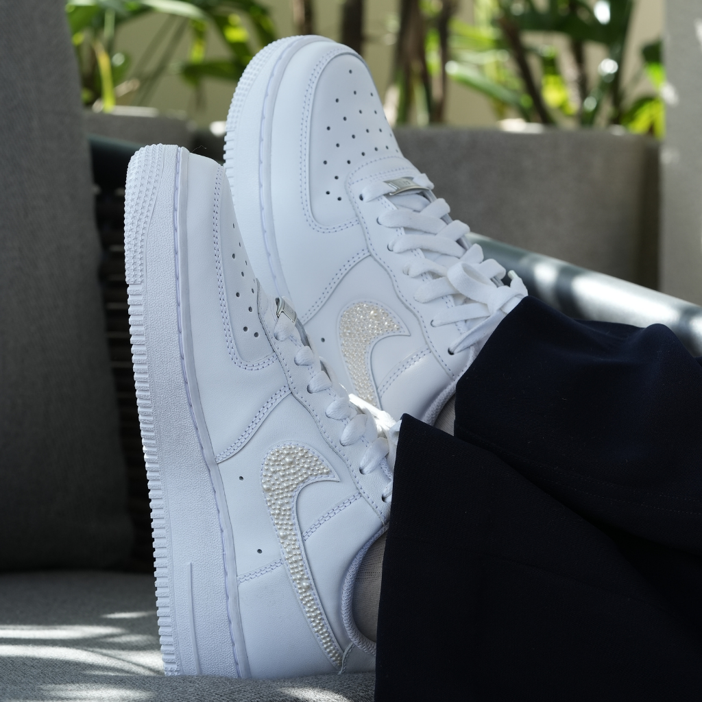 White designer sneakers with crystal-studded swoosh, worn outdoors, streetwear style
