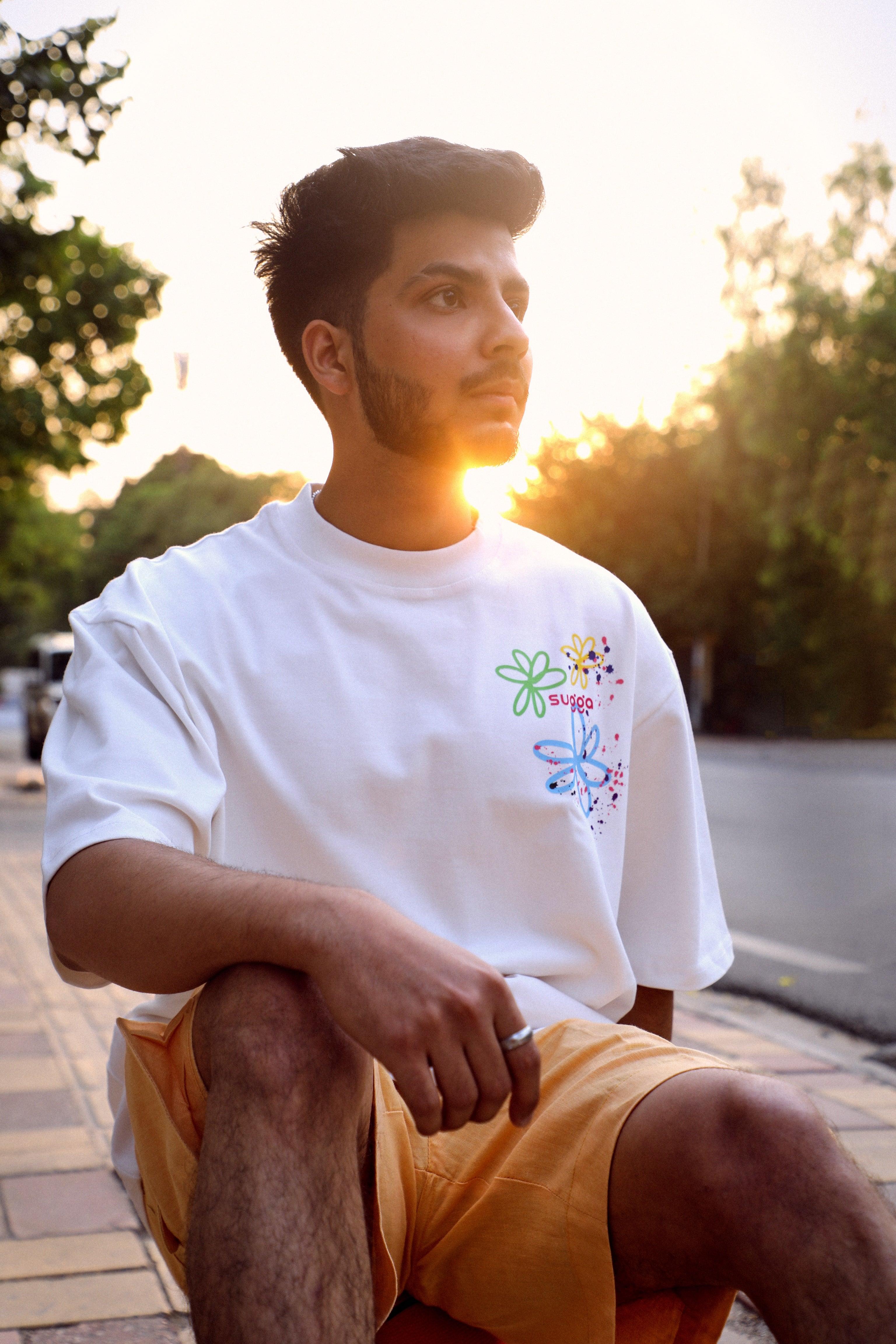 Man wearing a white streetwear t-shirt with colorful floral print and yellow shorts at sunset