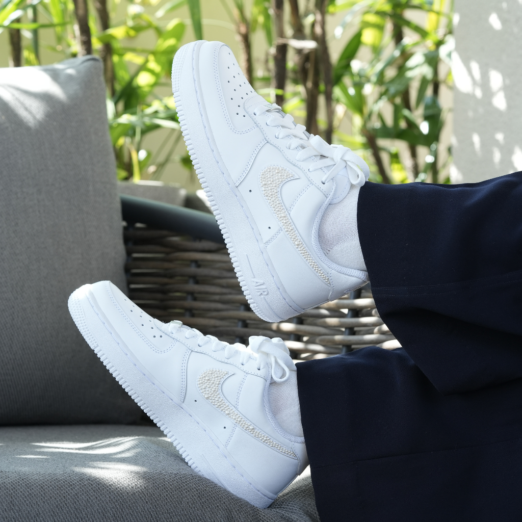 White low-top streetwear sneakers with textured swoosh, worn outdoors on a patio chair