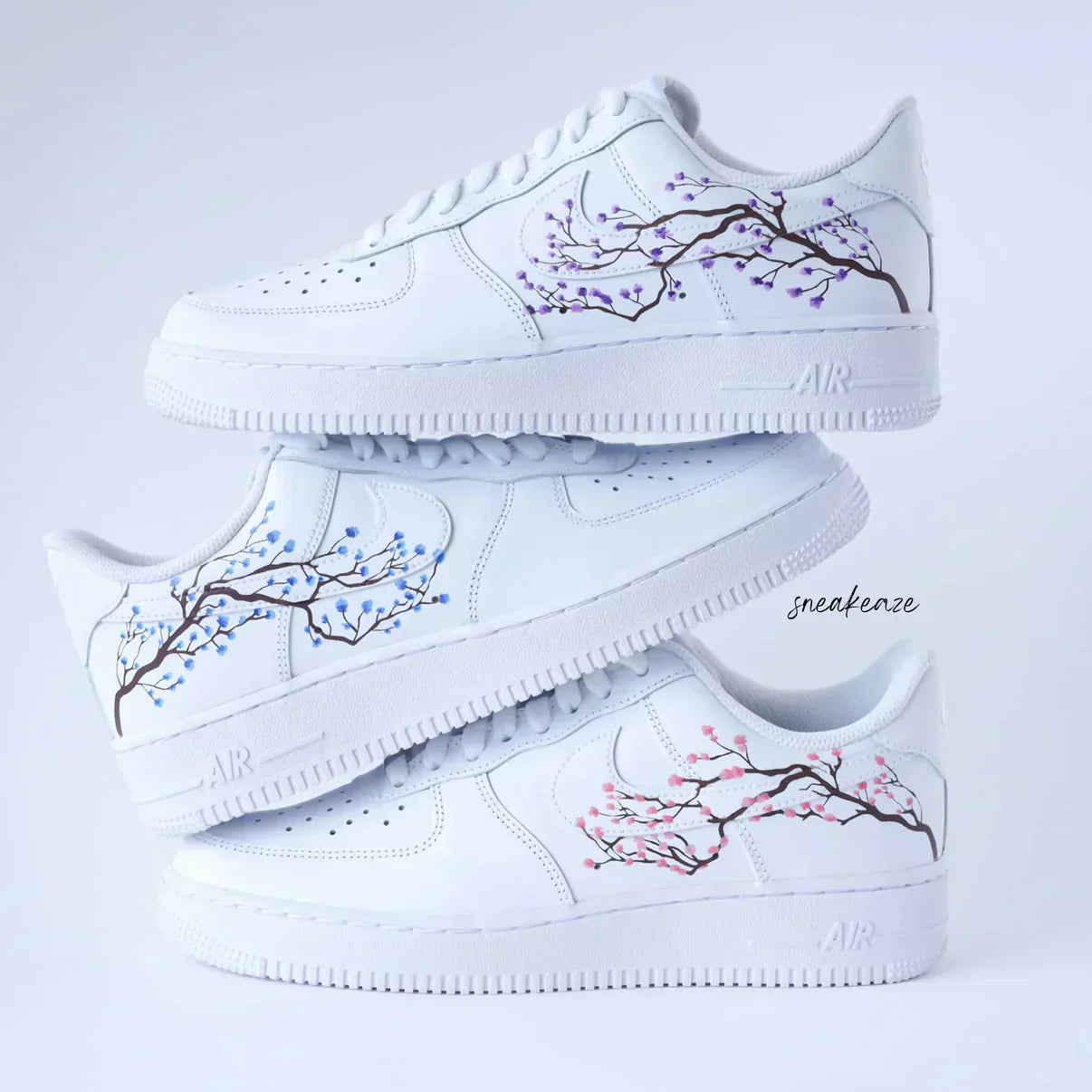 White custom sneakers stacked with hand-painted cherry blossom branch designs in blue, purple, and pink.