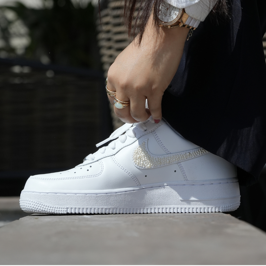 White designer sneaker with pearl-decorated swoosh worn by a person with gold rings