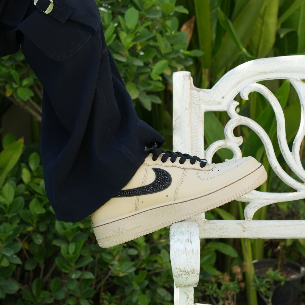 Beige Nike Air Force 1 sneaker with black swoosh worn outdoors, streetwear fashion style