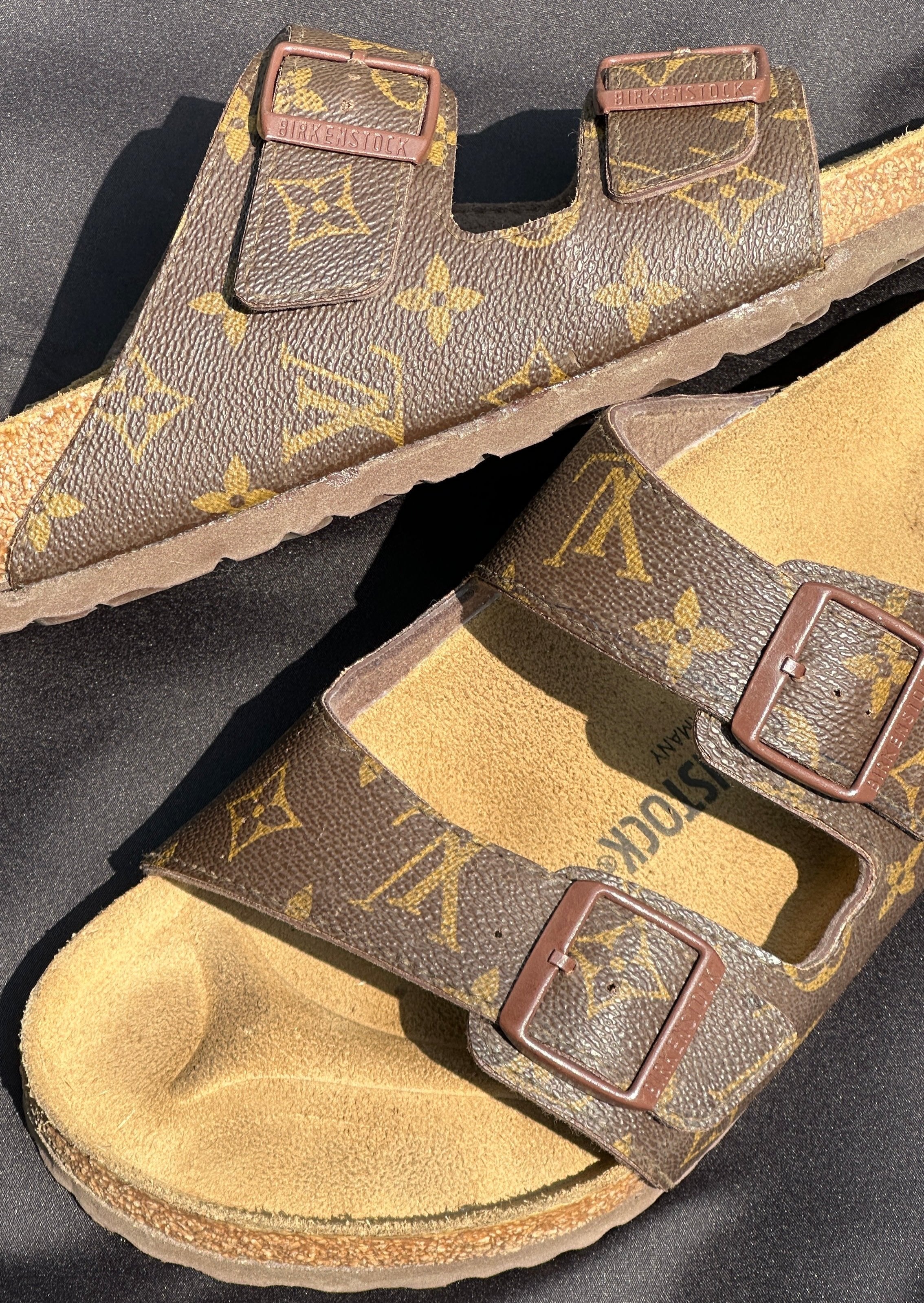 Brown Birkenstock sandals with monogram pattern, double straps and metal buckles on black background