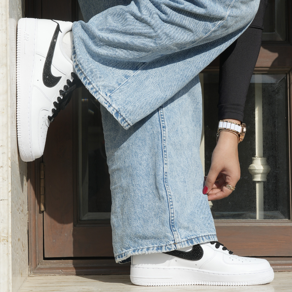 White streetwear sneakers with black swoosh, worn with wide-leg jeans and a black long sleeve top.