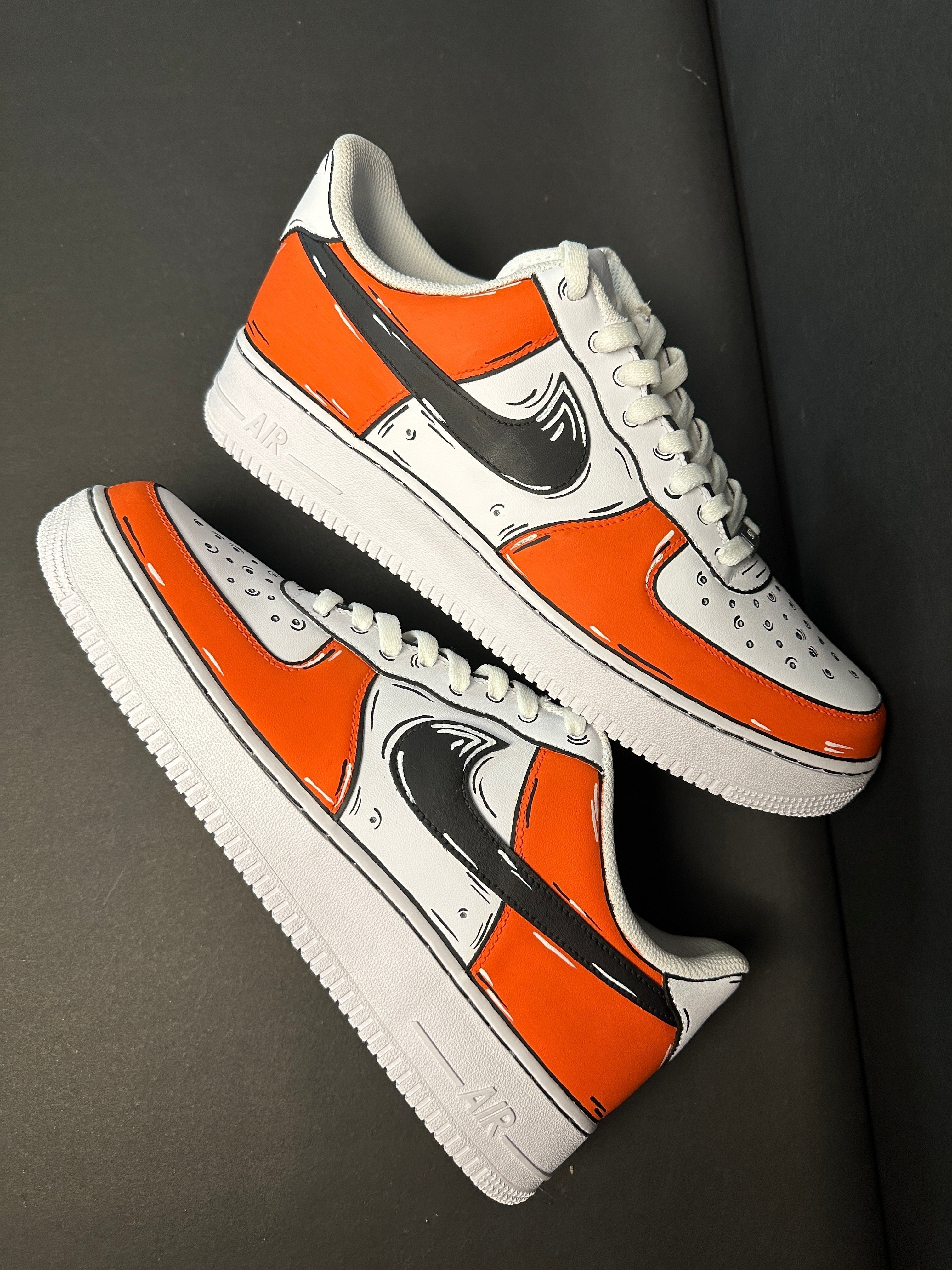 Custom white and orange streetwear sneakers with bold black graphic detailing on a dark background.