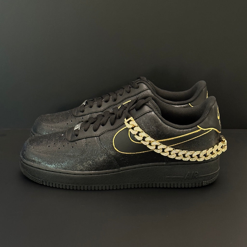 Black Nike Air Force 1 sneakers with gold outline and gold chain accent on side