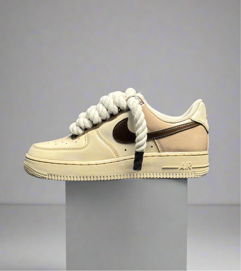 Beige and brown streetwear sneaker with thick rope laces on a minimal pedestal display.