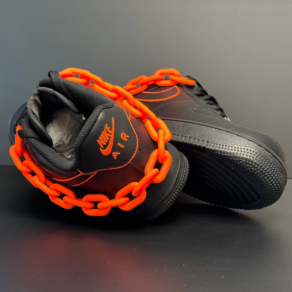 Black Nike Air Force 1 sneakers with bold orange accents and a chunky orange chain.