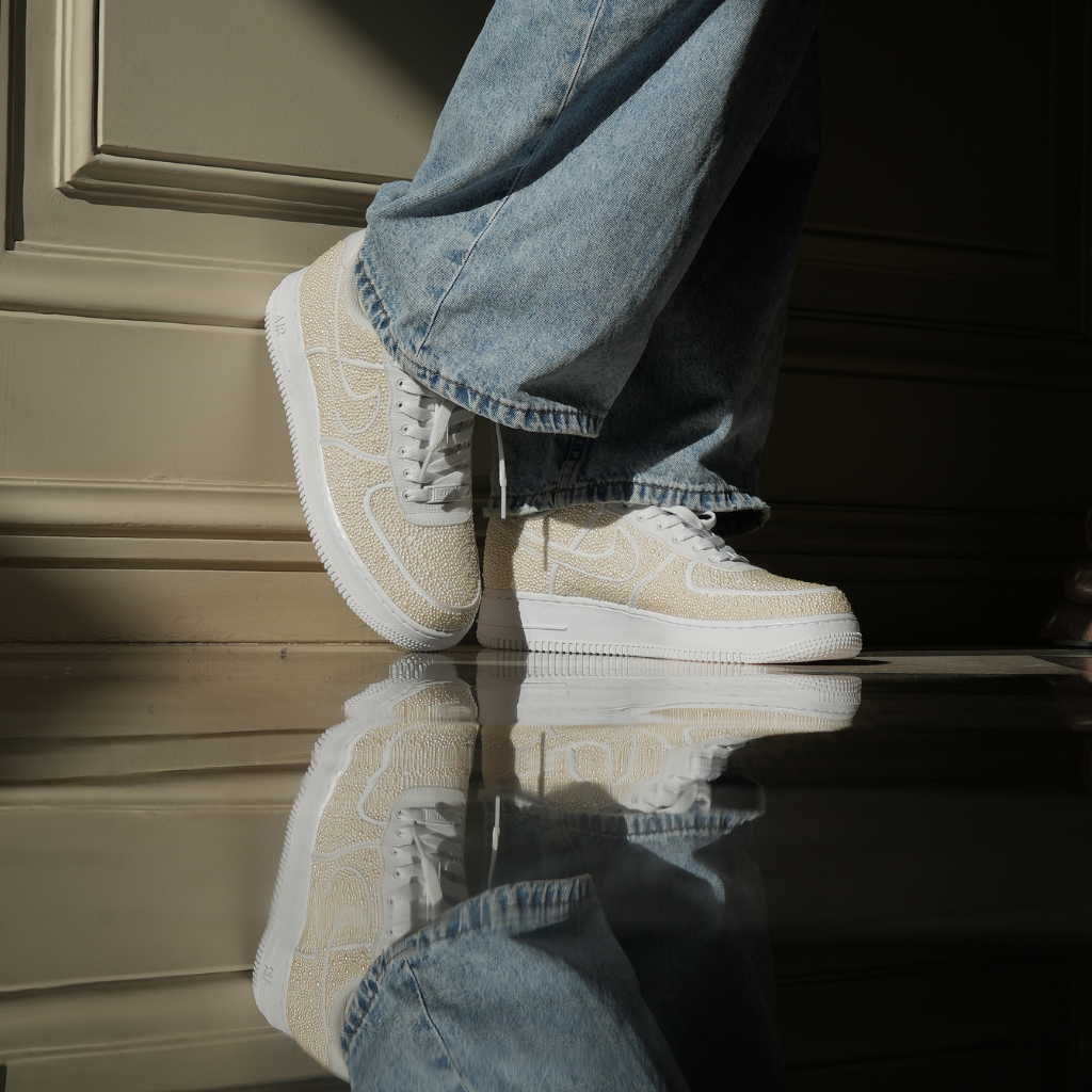 Beige textured designer sneakers with white soles worn with baggy denim jeans, reflected on floor