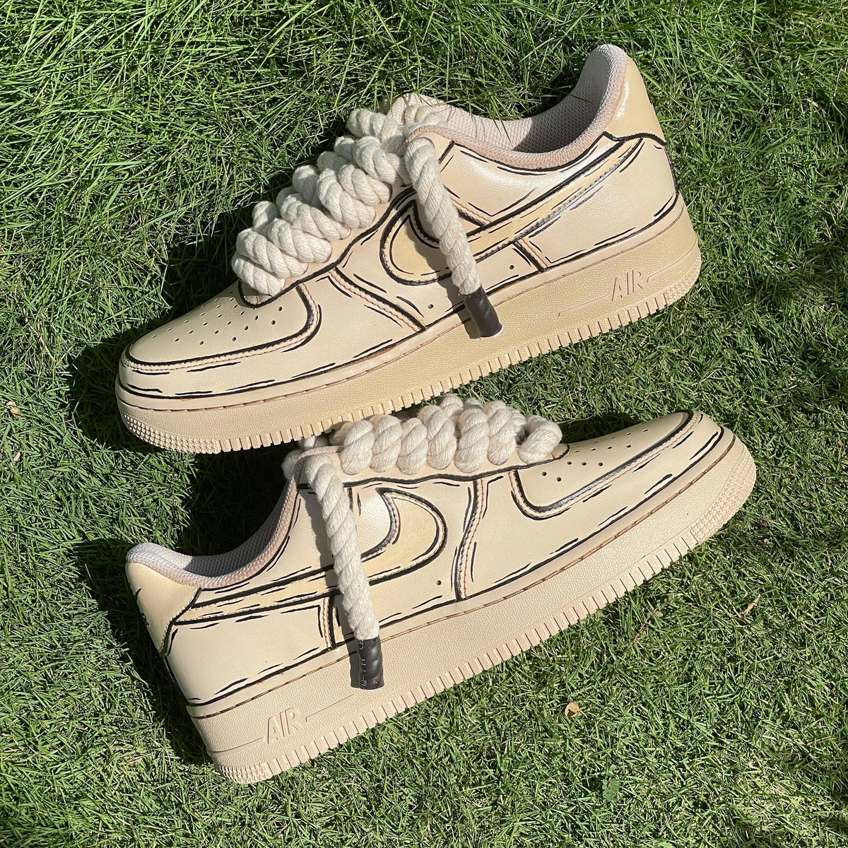 Beige streetwear sneakers with thick rope laces and black sketch detailing on grass