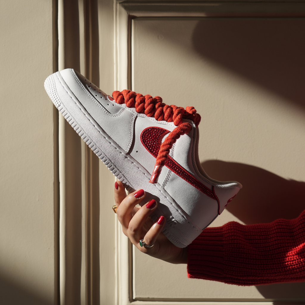 White and red streetwear sneaker with thick red laces held by person in a red sweater