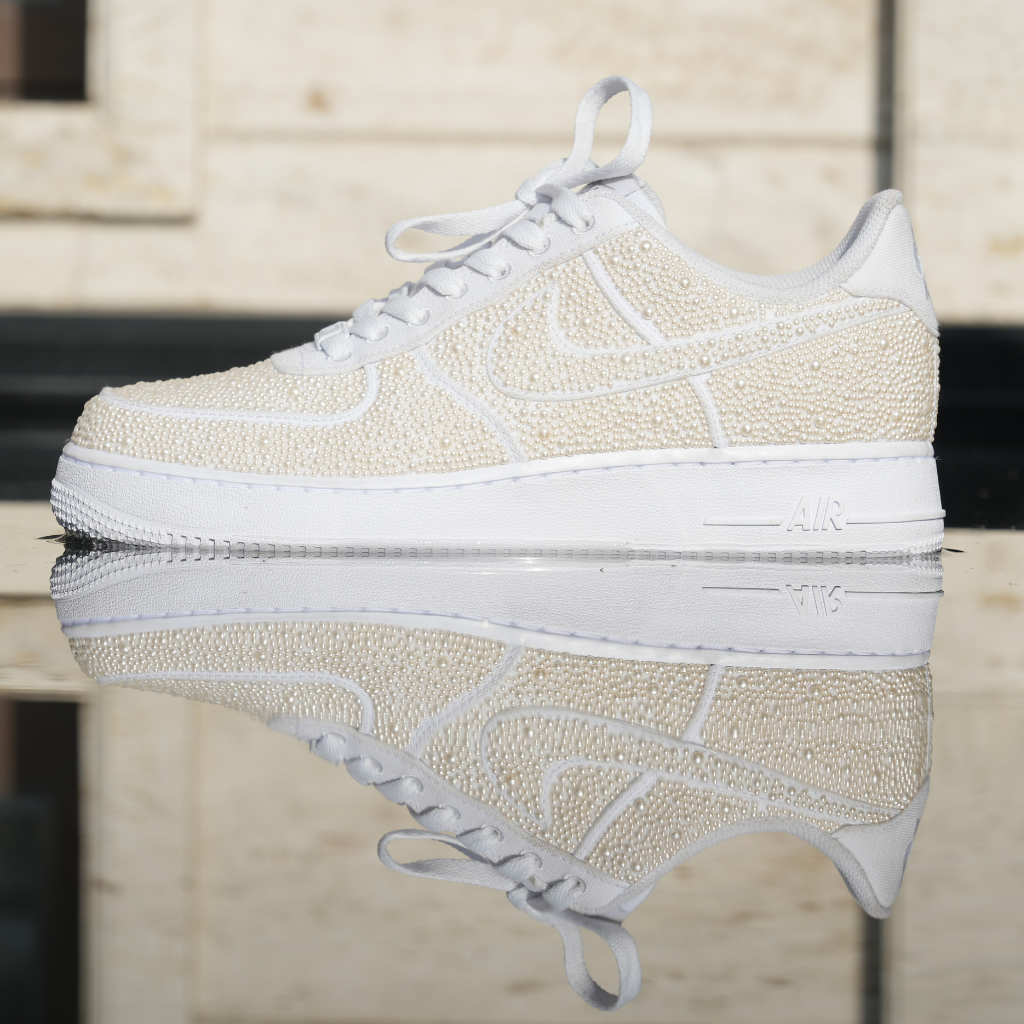White designer sneaker with pearl embellishments and reflective sole on urban background