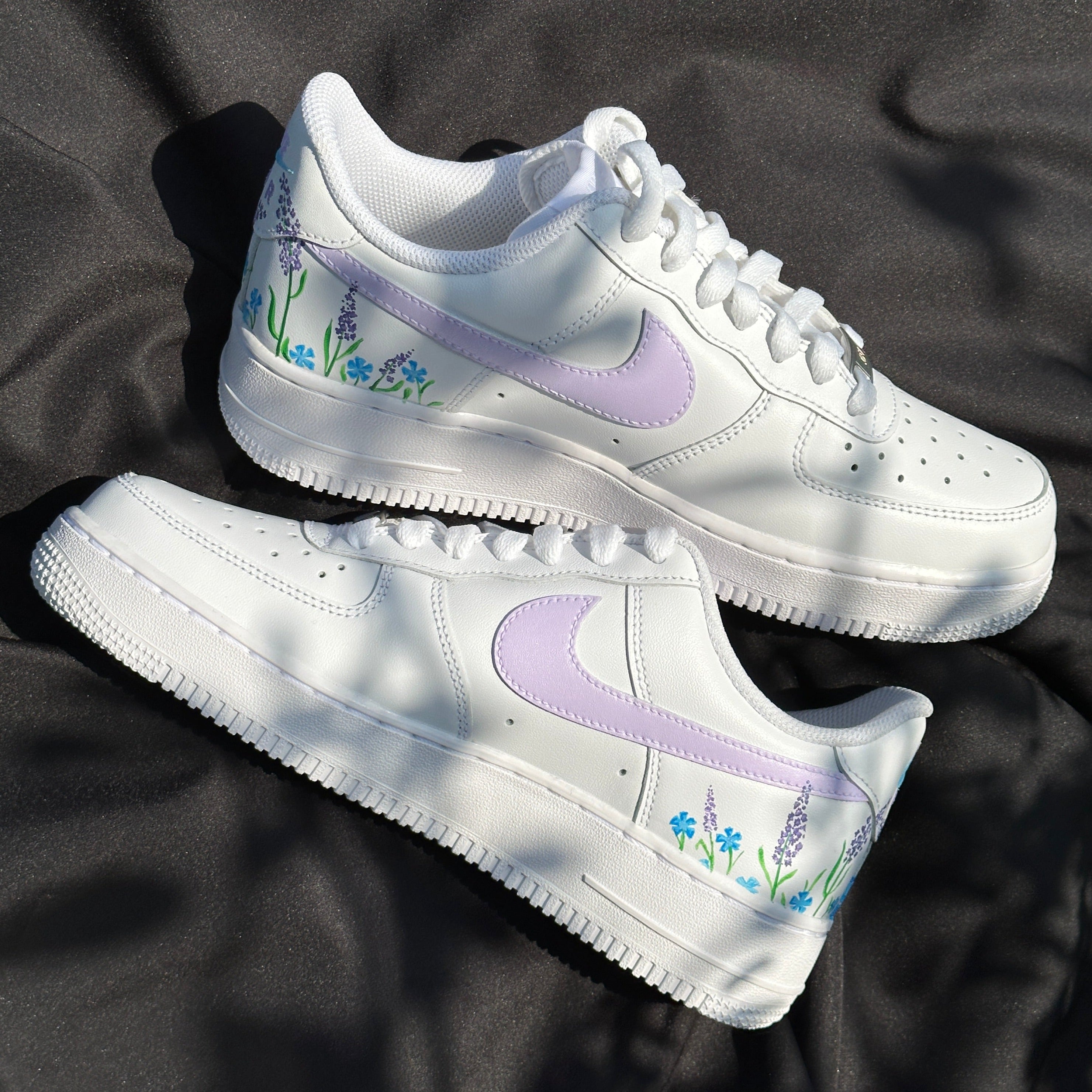 White sneakers with pastel purple swoosh and blue floral designs, streetwear style.