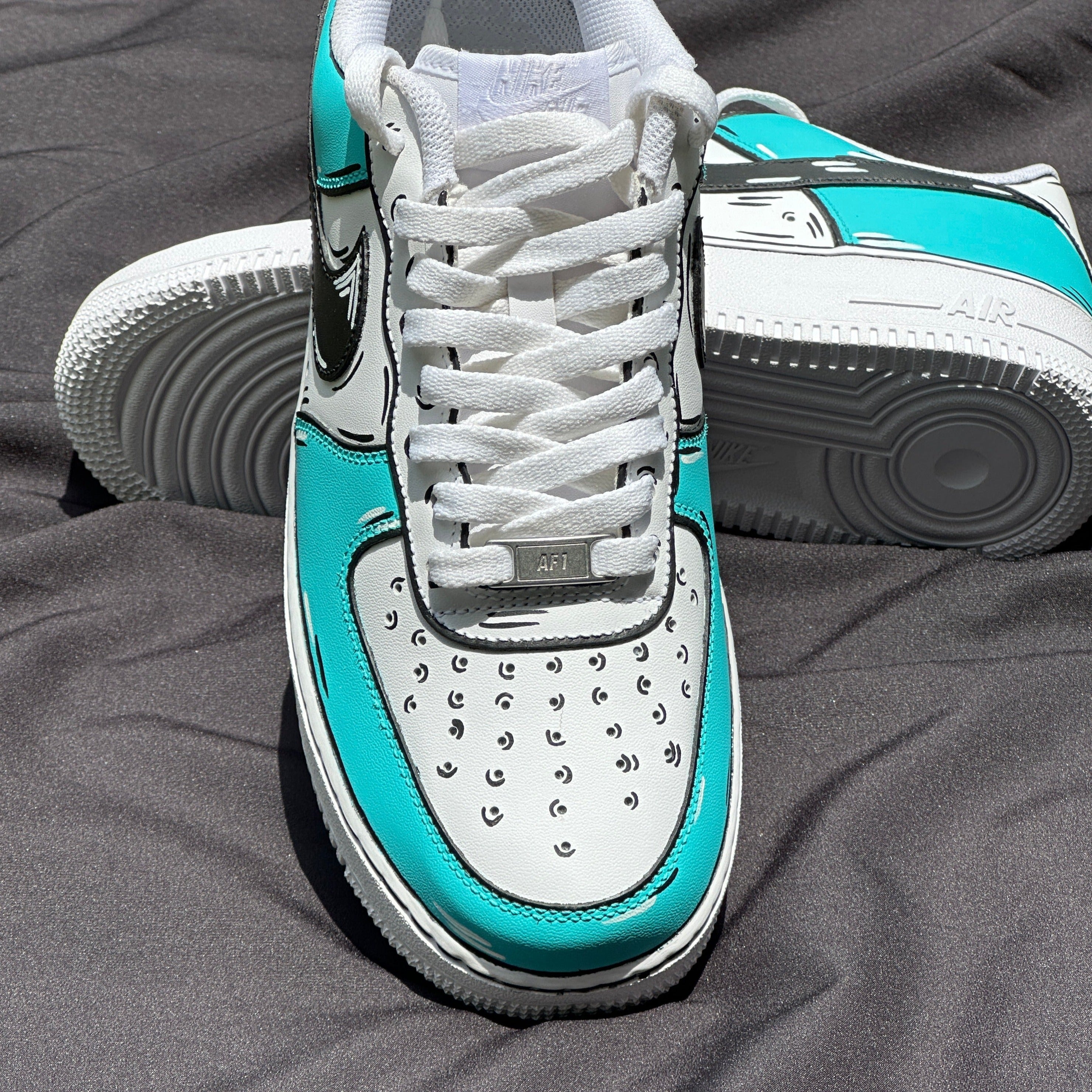 White and turquoise streetwear sneakers with cartoon-style accents on a dark fabric background.