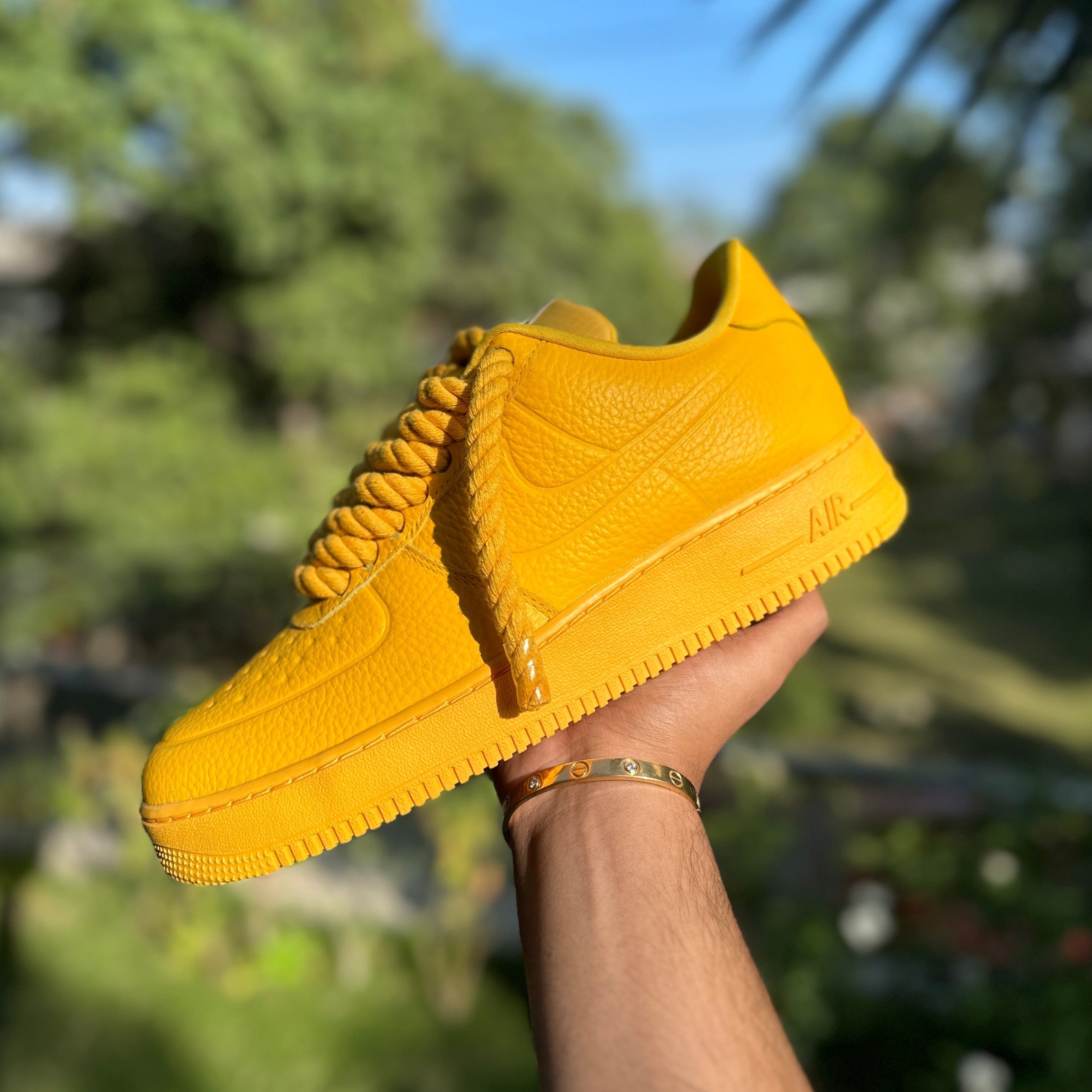 Yellow leather streetwear sneaker with textured finish and chunky laces held outdoors