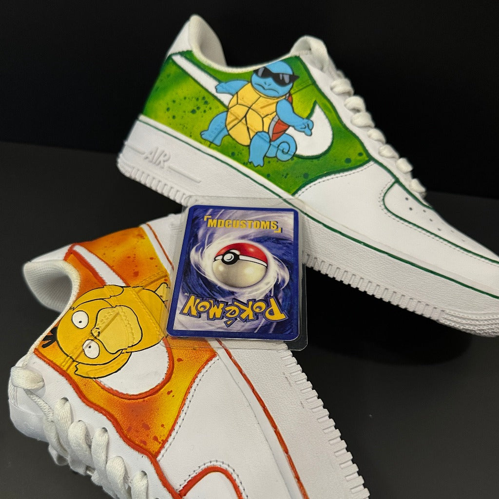 Custom white sneakers with colorful hand-painted Pokémon designs, featuring Squirtle and Psyduck, and a Pokémon trading card placed between the shoes on a black background.