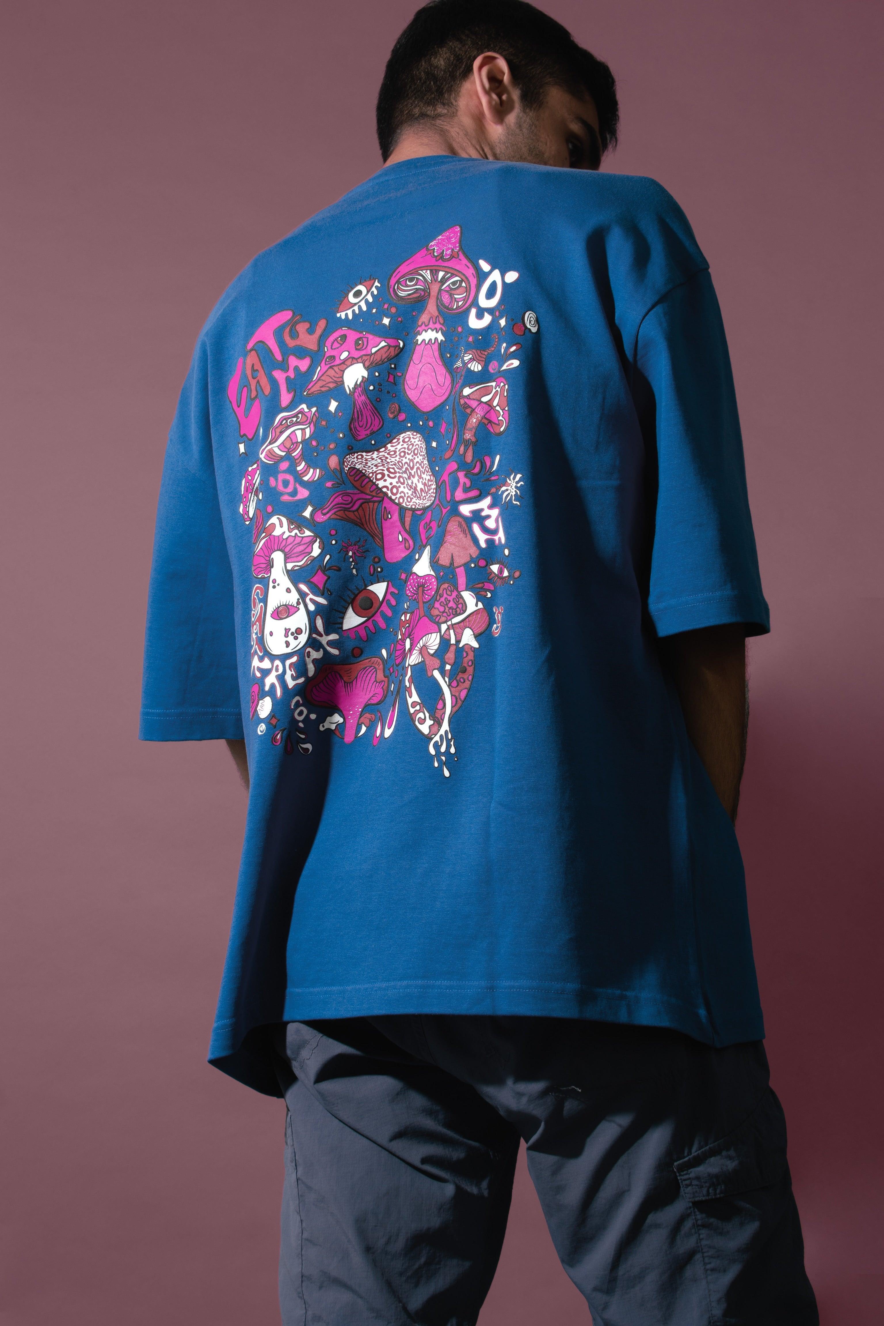 Man in blue graphic streetwear t-shirt with colorful mushrooms and 'EAT ME' artwork on back