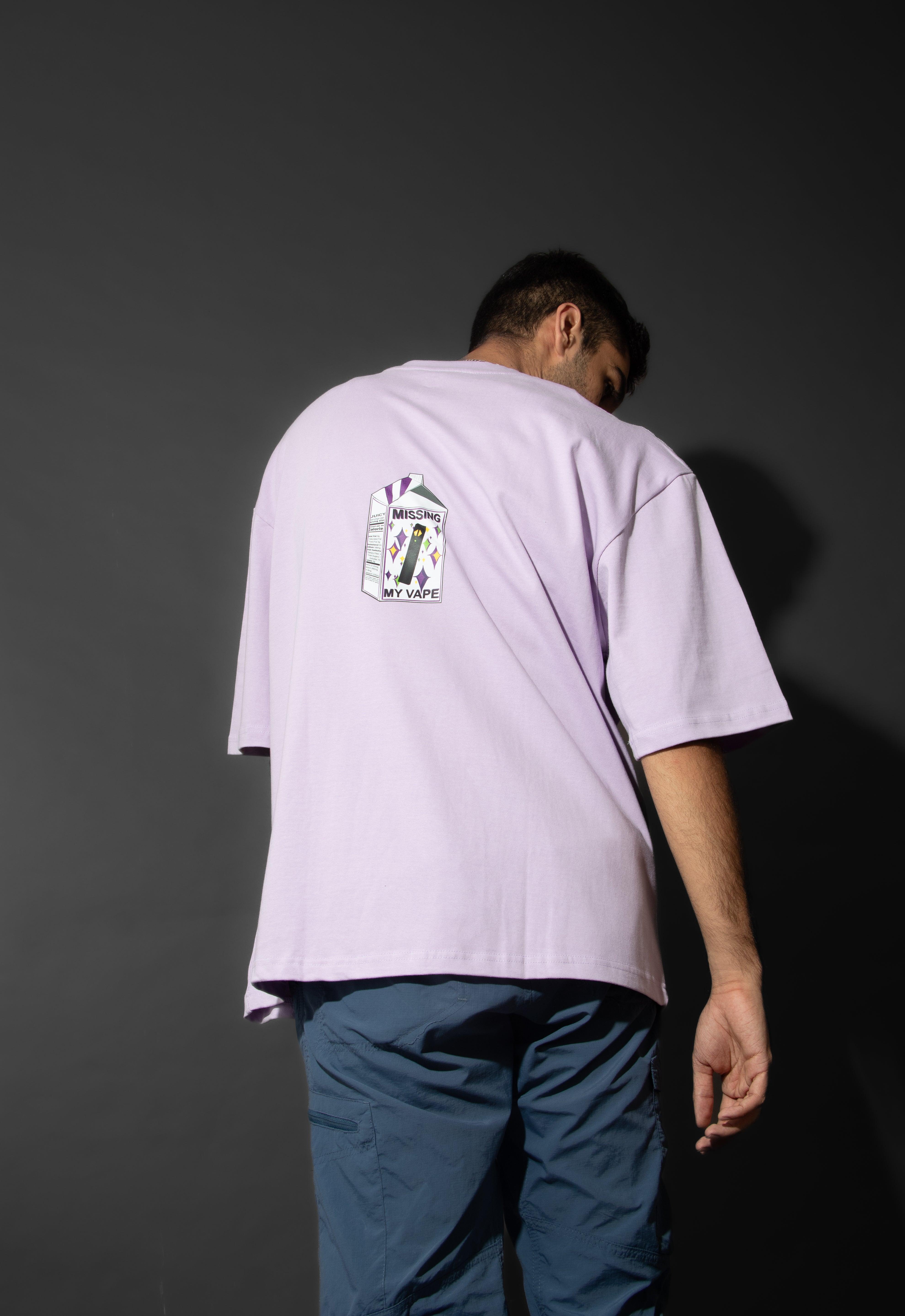 Man in lavender streetwear t-shirt with 'Missing My Vape' cartoon graphic on back, dark background