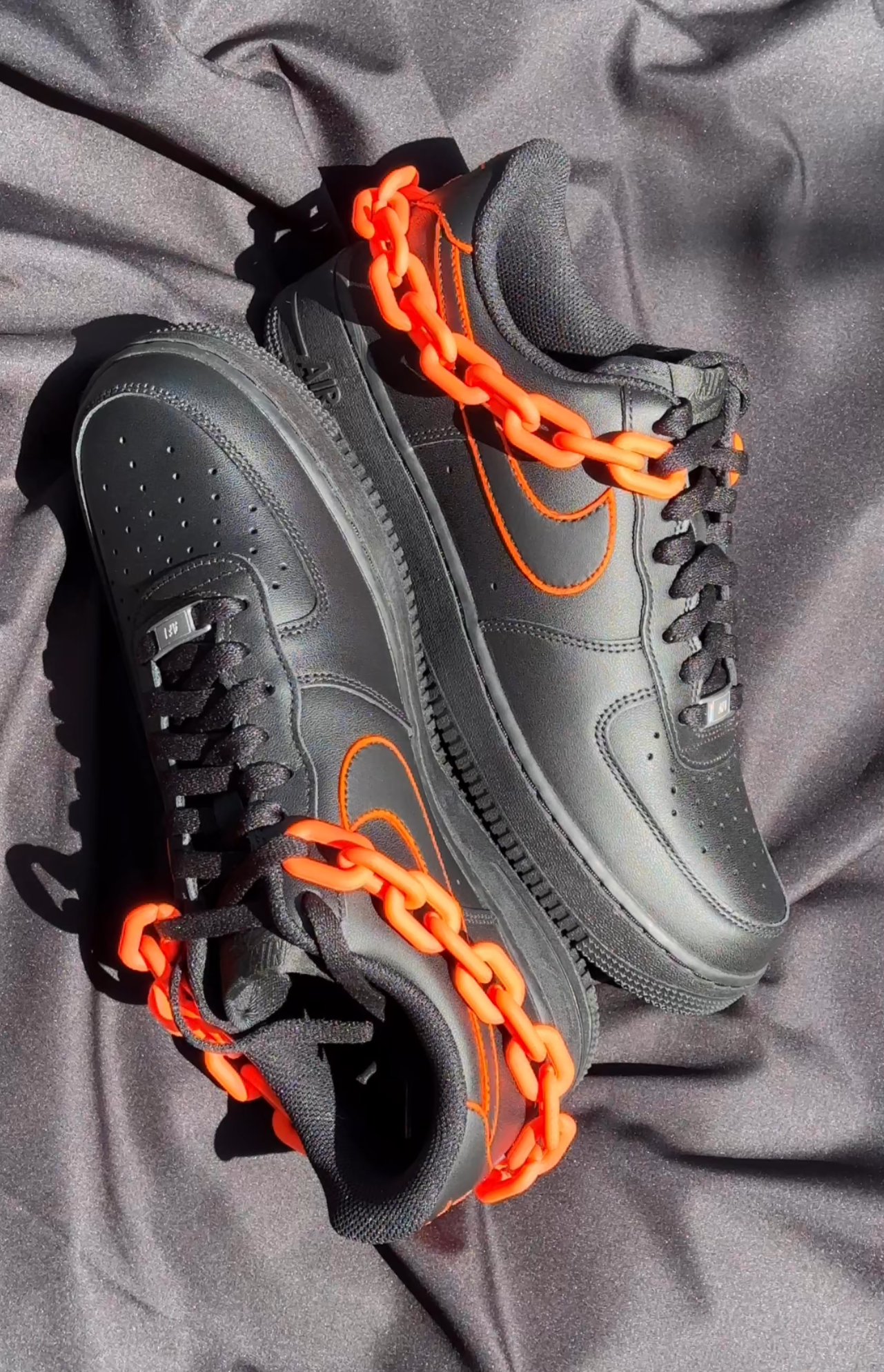 Black streetwear sneakers with orange accents and chunky orange chain on silky fabric