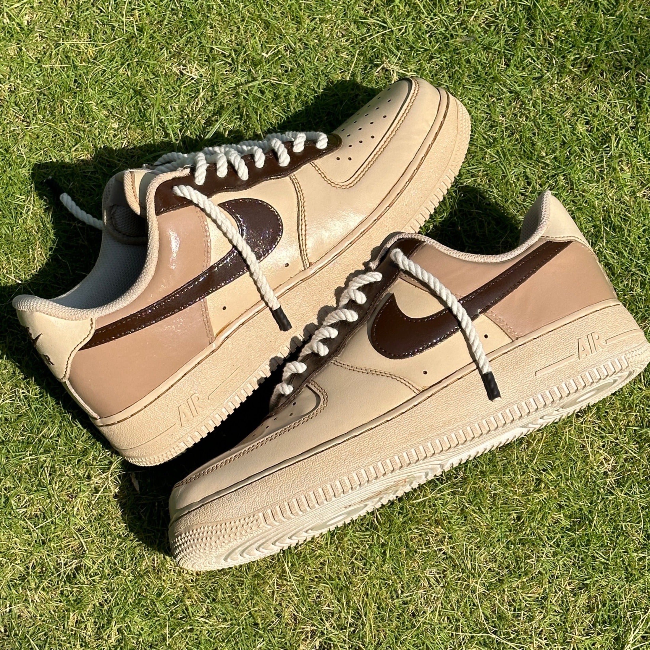 Beige and brown Nike Air Force 1 sneakers with white rope laces on grass, stylish streetwear footwear