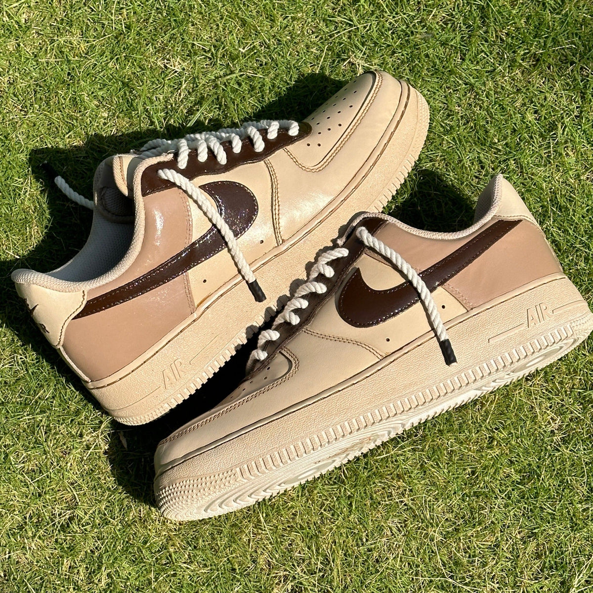 Beige and brown Nike Air Force 1 sneakers with white rope laces on grass, stylish streetwear footwear