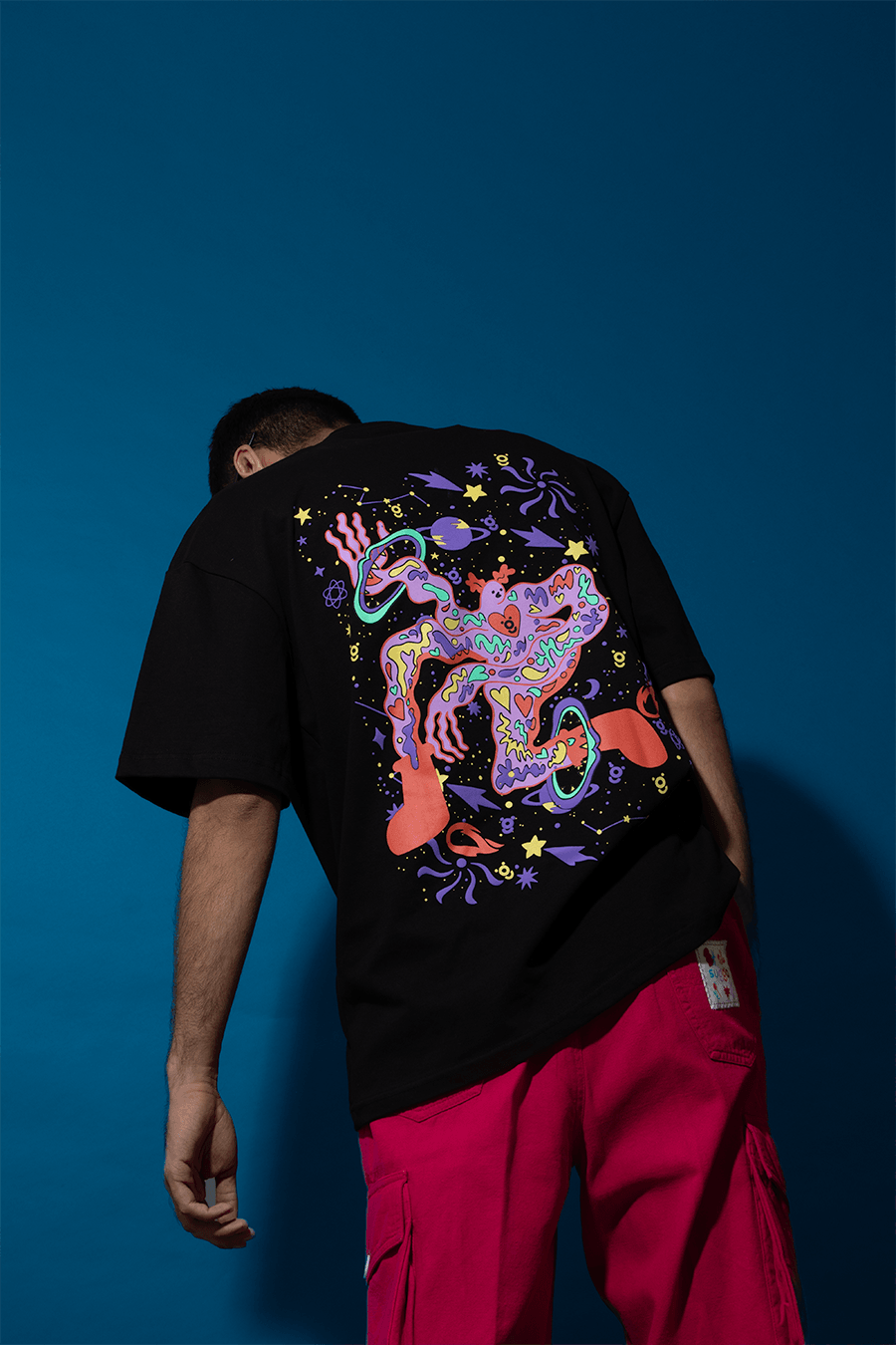 Man wearing black graphic streetwear t-shirt with colorful abstract design, red cargo pants
