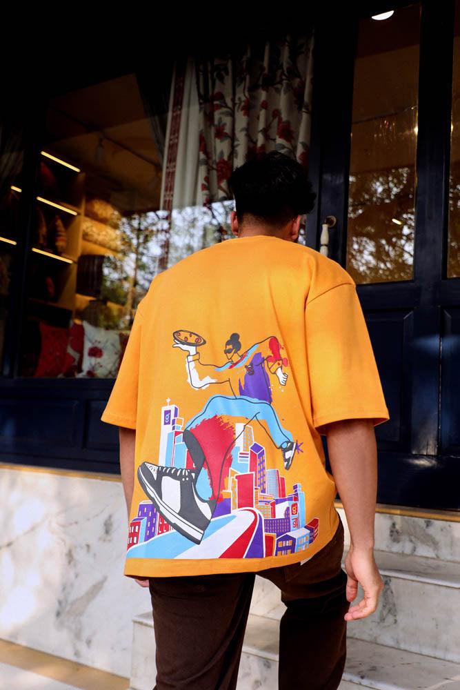 Man wearing yellow streetwear t-shirt with colorful graphic print, standing outside shop