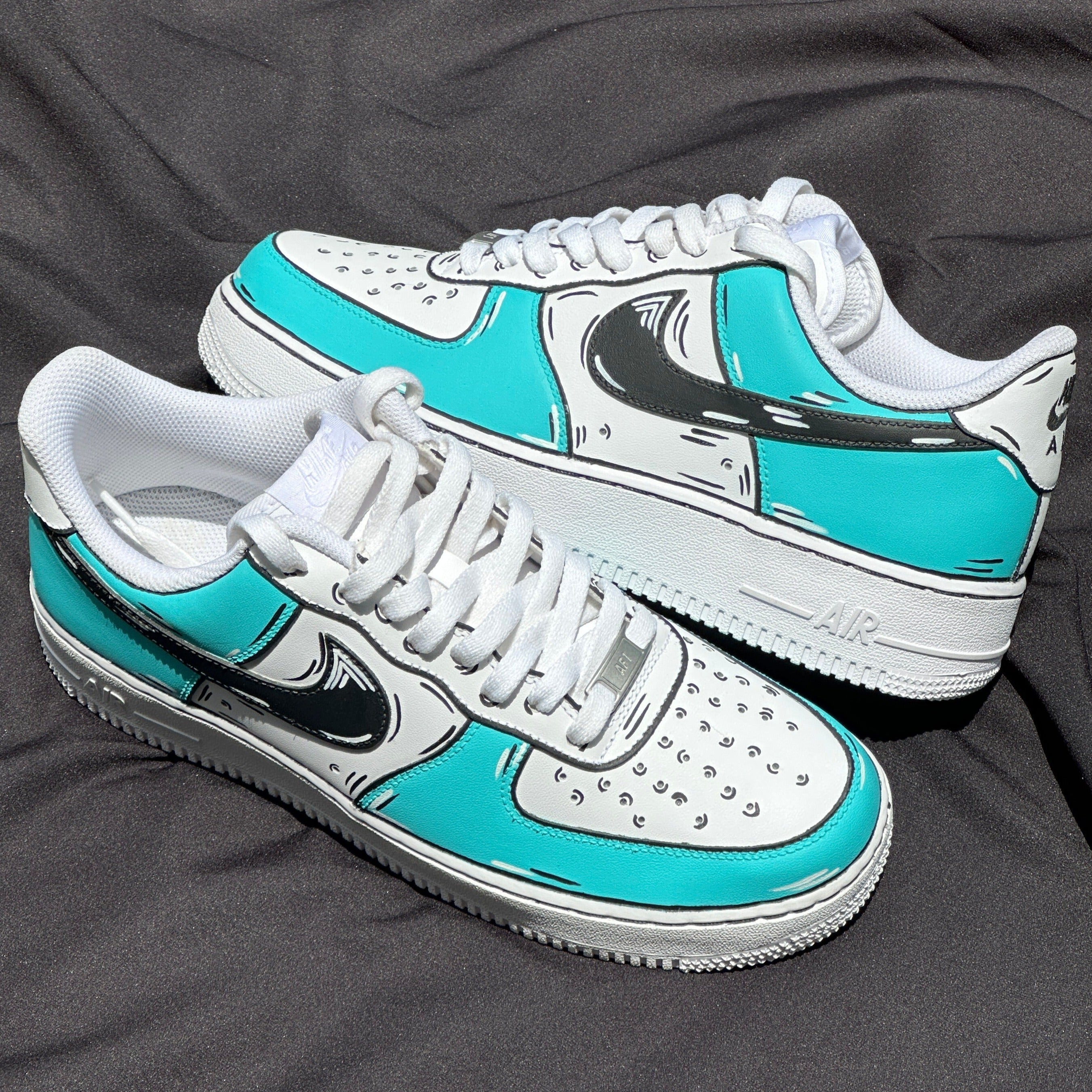 Turquoise and white streetwear sneakers with black graphic accents on a dark cloth background
