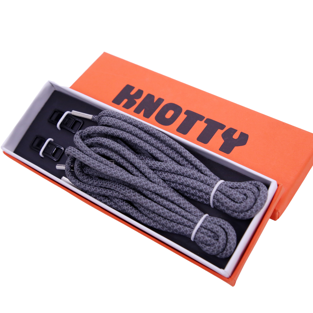 A set of reflective shoelaces and a premium metal dubrae tag, packaged together with the brand name 'KNOTTY' printed on an orange and black box.